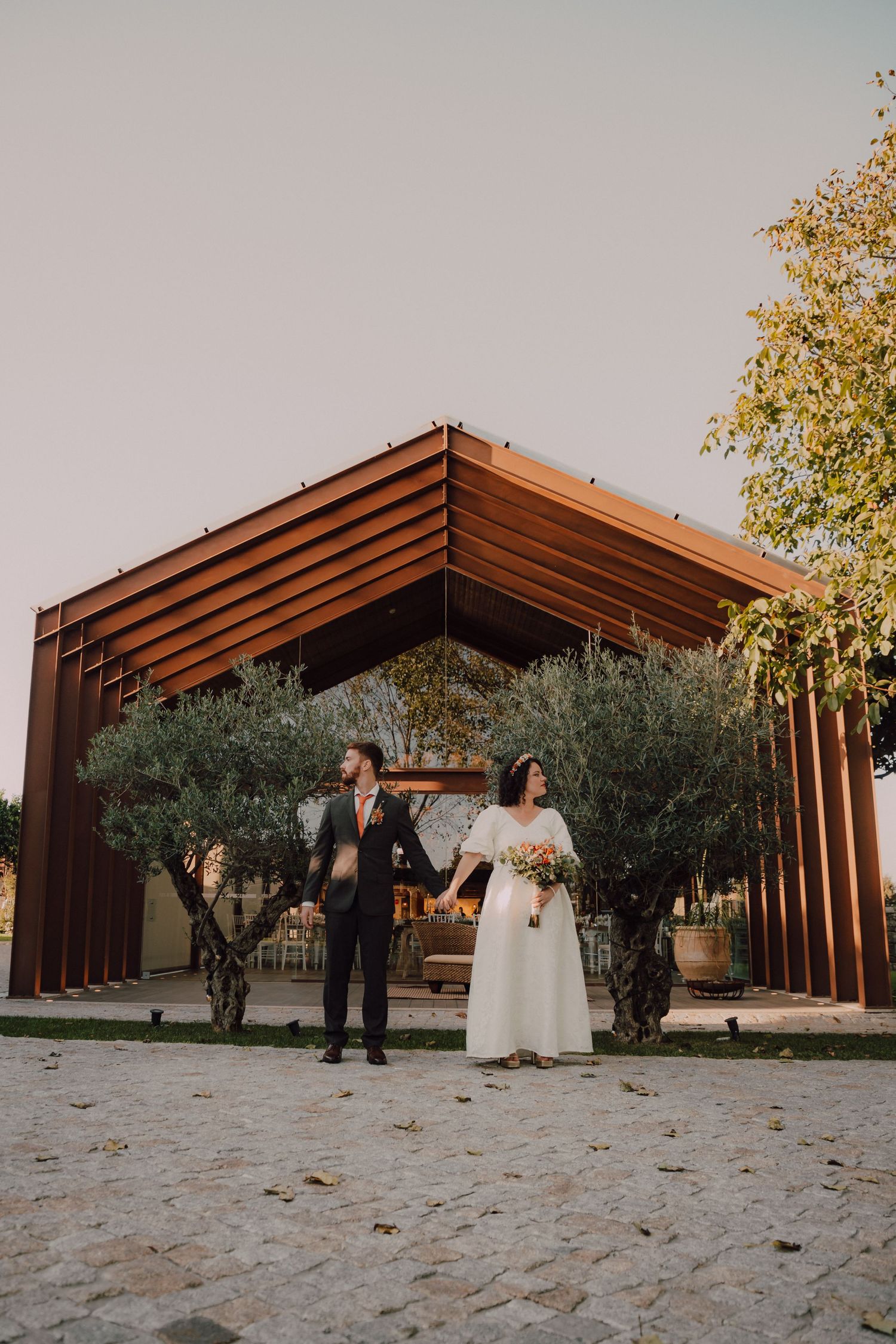 A modern wooden pergola surrounded by olive trees creates an elegant outdoor wedding setting.