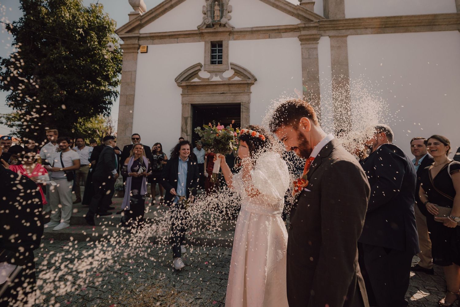 A couple celebrates outside a church while guests shower them with confetti.