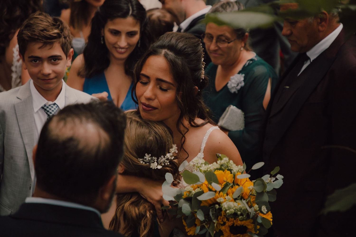 Wedding celebration with guests gathered around bouquets of sunflowers in an outdoor setting.