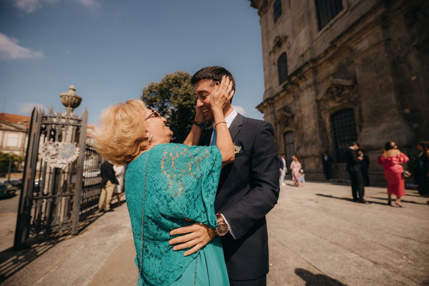 Couple embracing outside historic stone building on sunny day.
