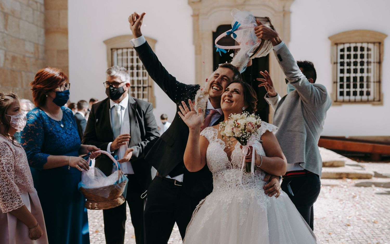 Wedding celebration outside a historic building with guests throwing confetti and cheering.
