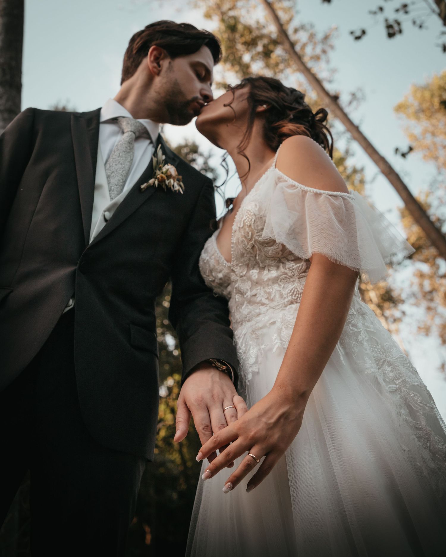 Romantic wedding portrait with couple embracing among tall trees at sunset.