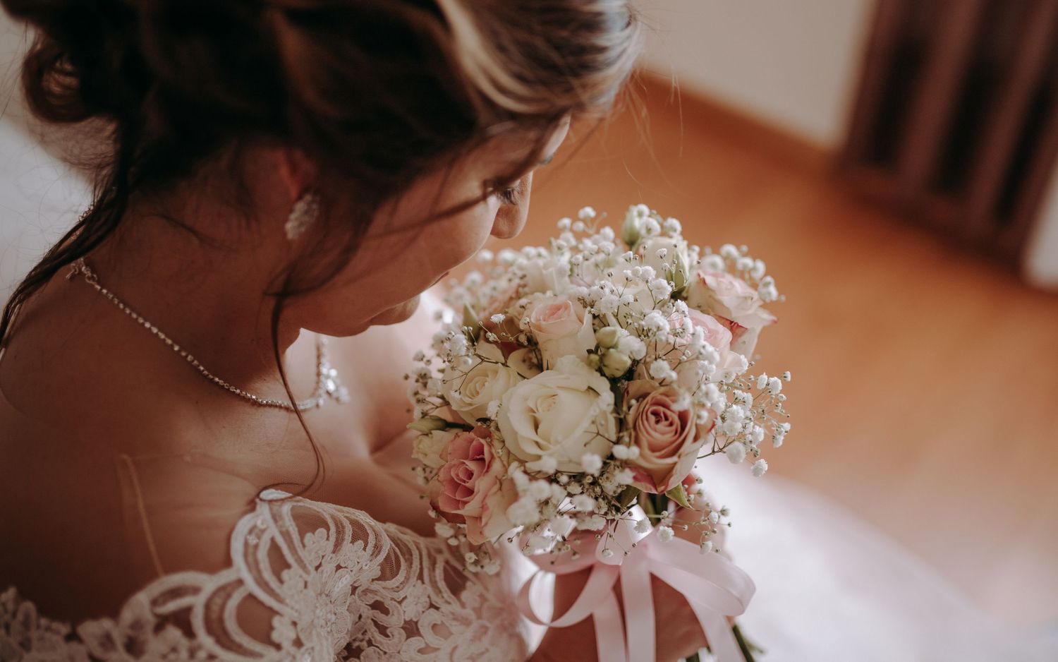 Soft focus image of bridal bouquet with pink and white roses against lace dress details.