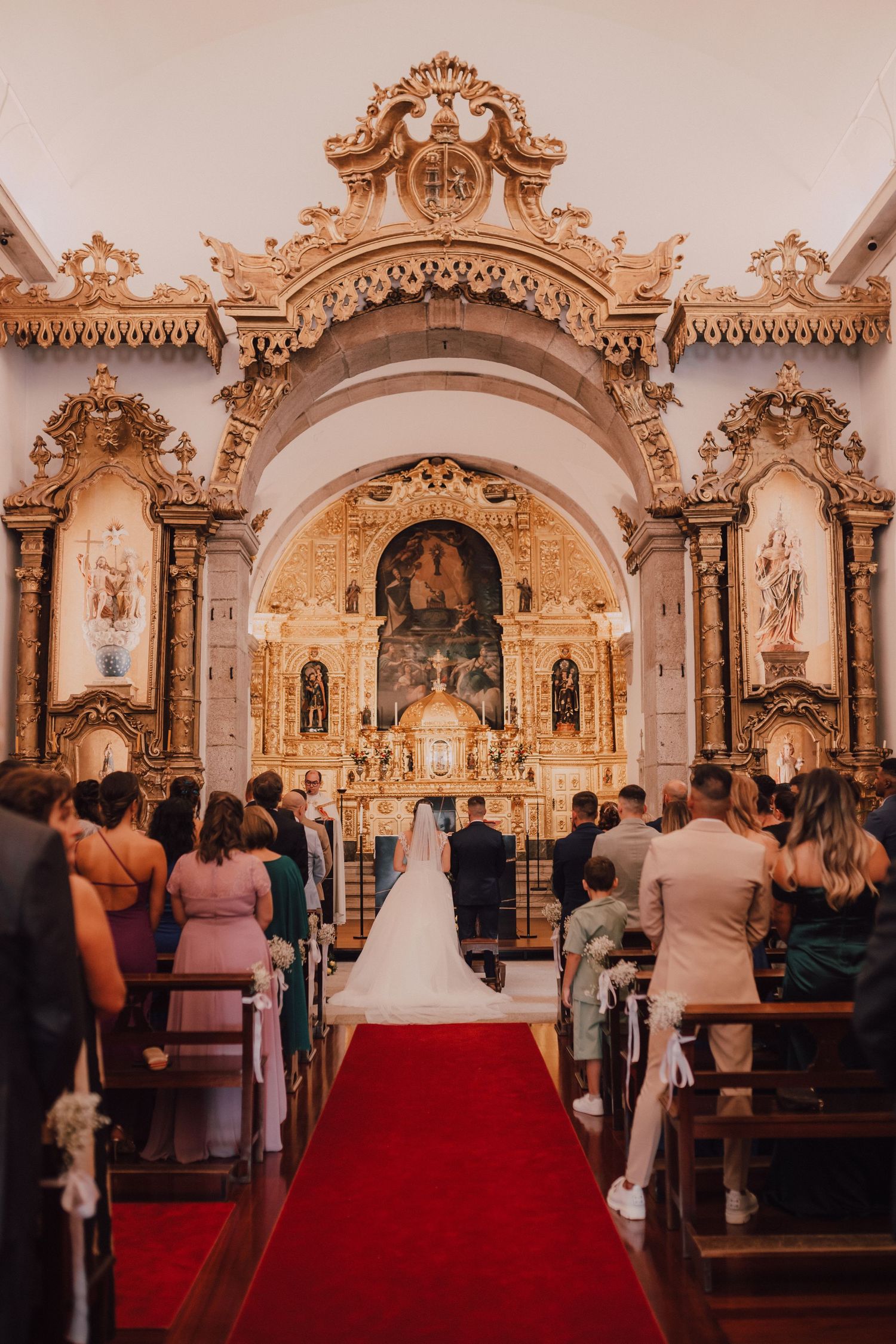 Ornate Catholic church interior with baroque altar and red carpet aisle during a traditional wedding ceremony.