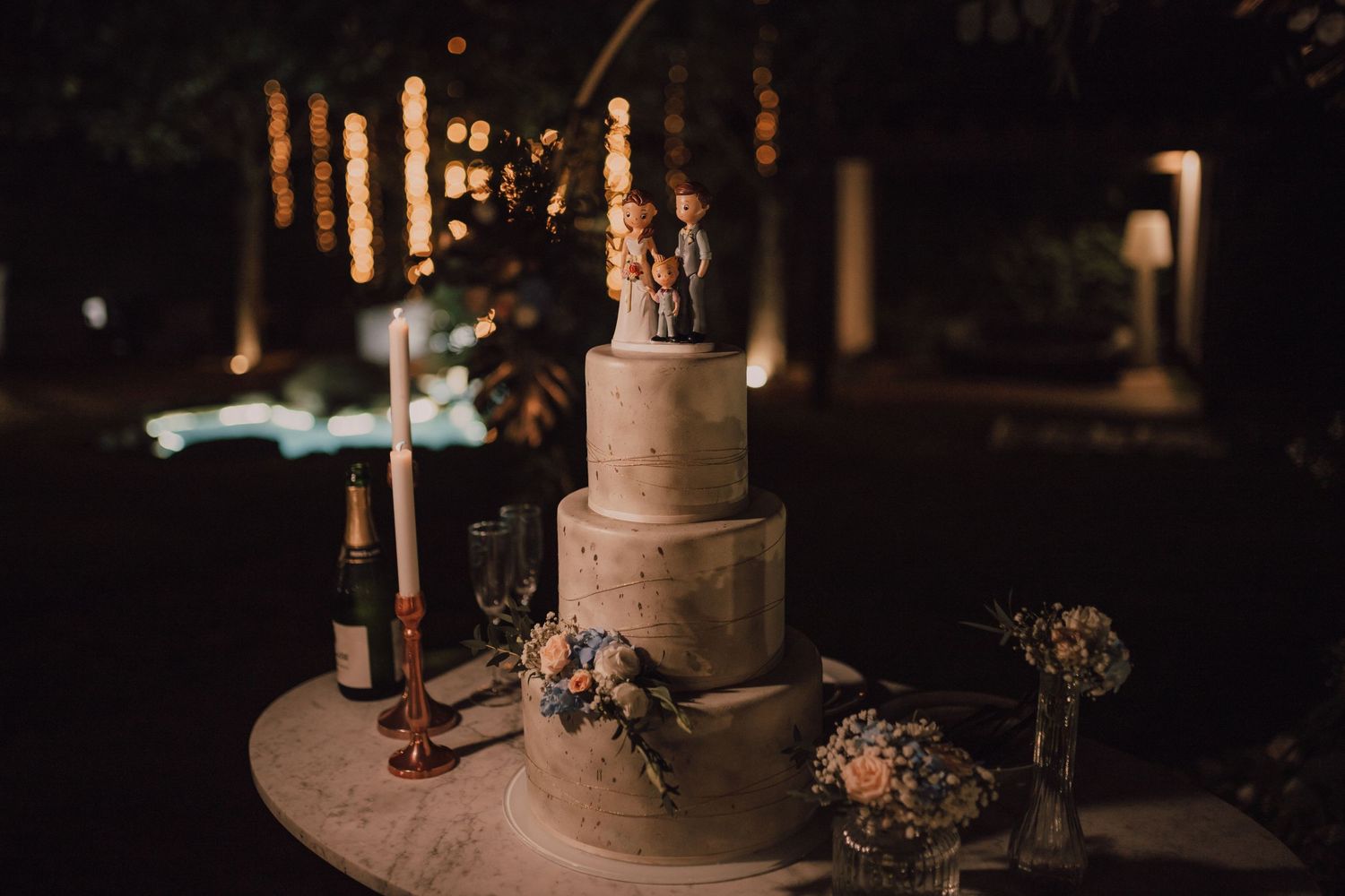 Elegant tiered wedding cake with floral decorations displayed in moody lighting.