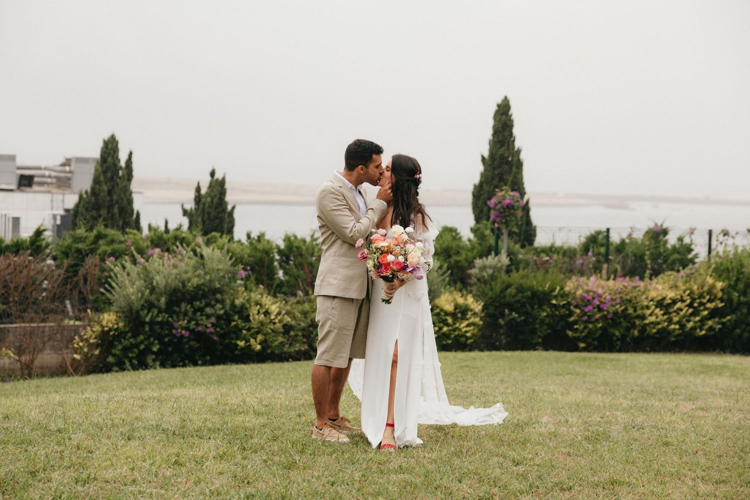 Couple embracing in garden setting with cypress trees and ocean view.