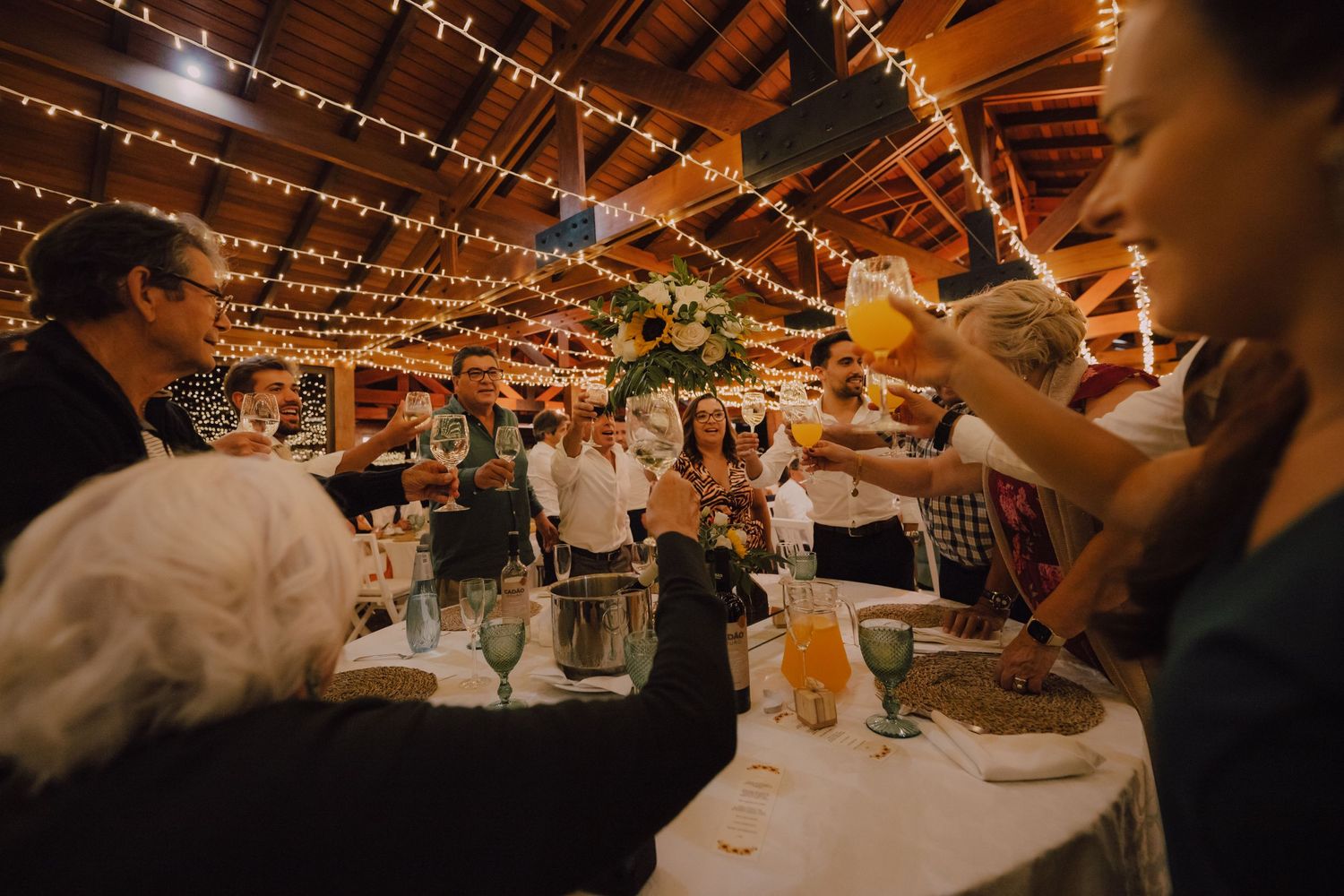 Wedding reception venue decorated with overhead string lights as guests celebrate at tables.