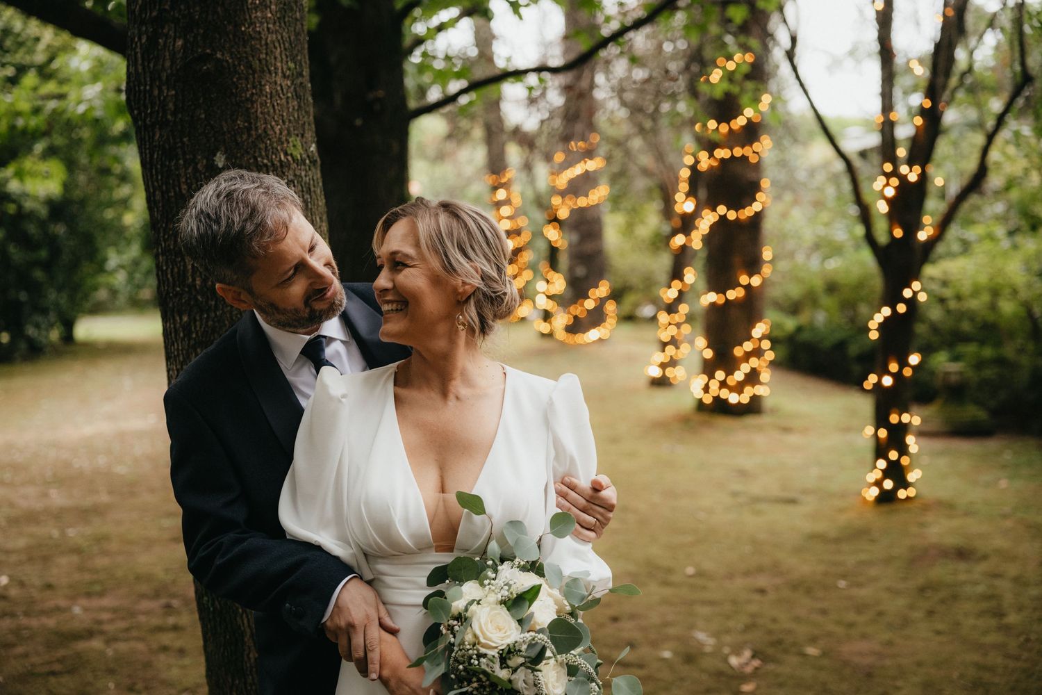 A romantic outdoor wedding moment with twinkle lights and trees in the background.