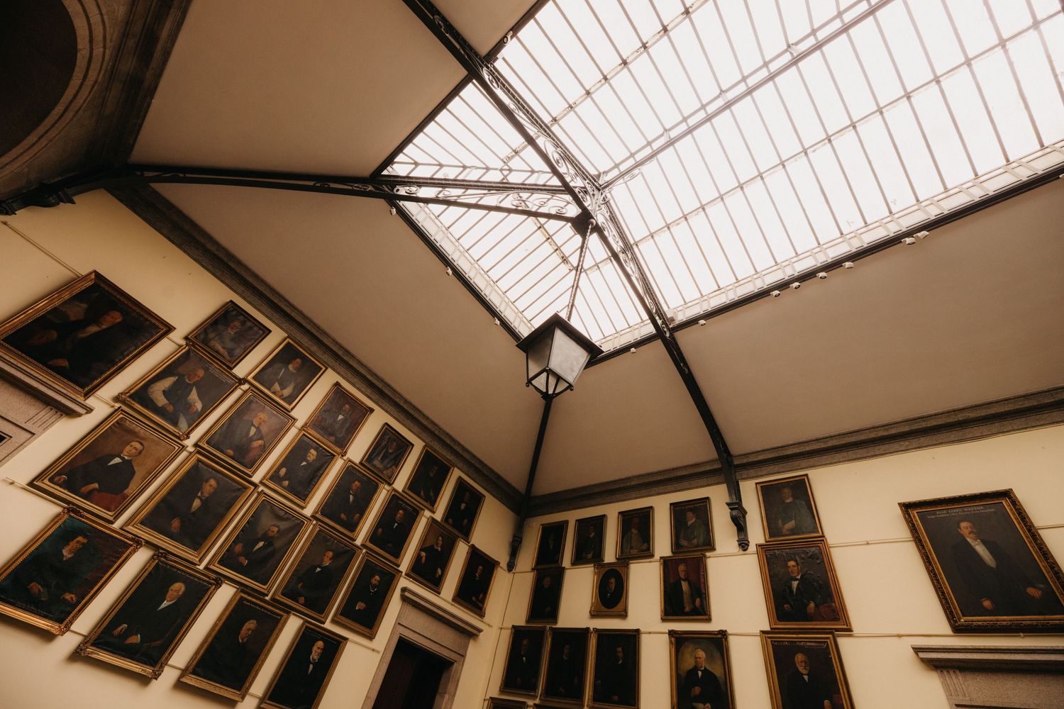 An architectural detail showing a skylight ceiling and walls lined with historic portrait paintings.