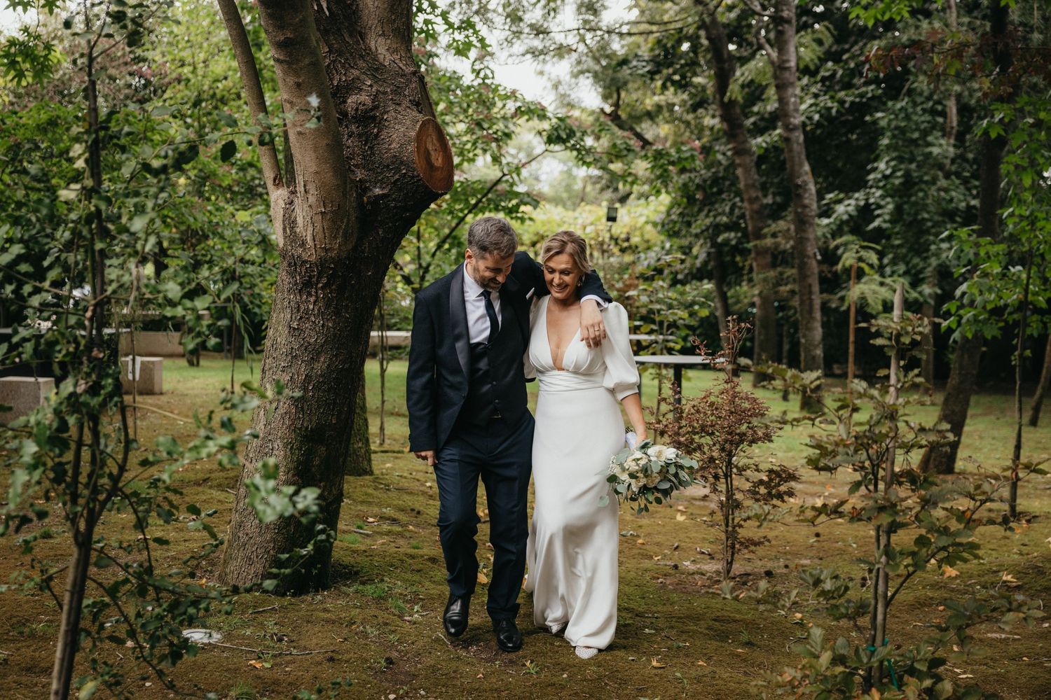 A couple walks together on their wedding day through a lush garden setting.