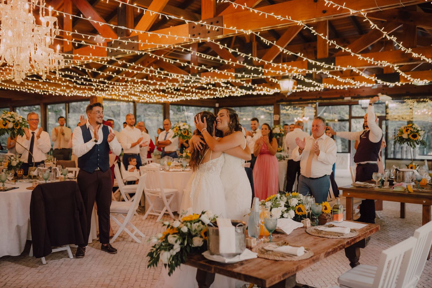 Wedding celebration in rustic venue with string lights and floral decorations.