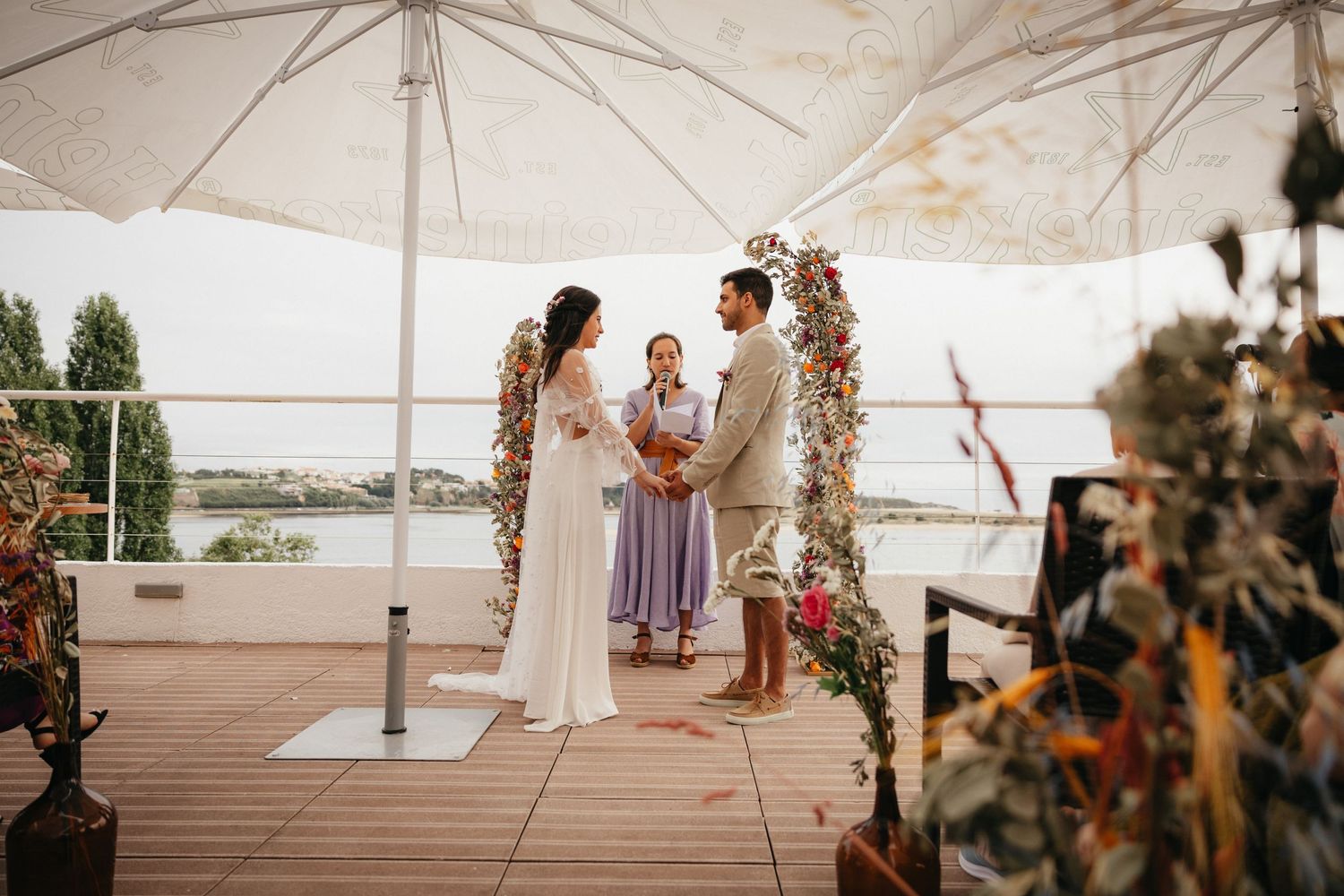 A beautiful outdoor wedding ceremony under a white tent with a floral arch and waterfront view.