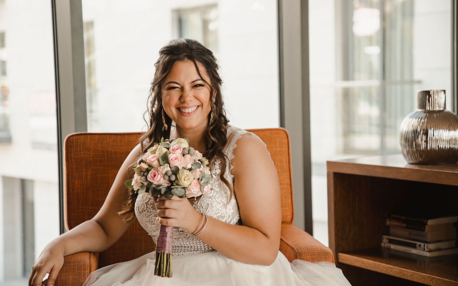 A person in white holding a pink and white floral bouquet sits in a leather chair.