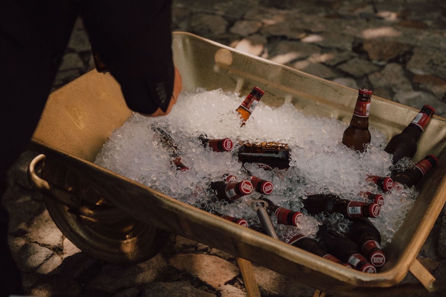 Ice-filled wooden box containing chilled wine bottles at outdoor event.
