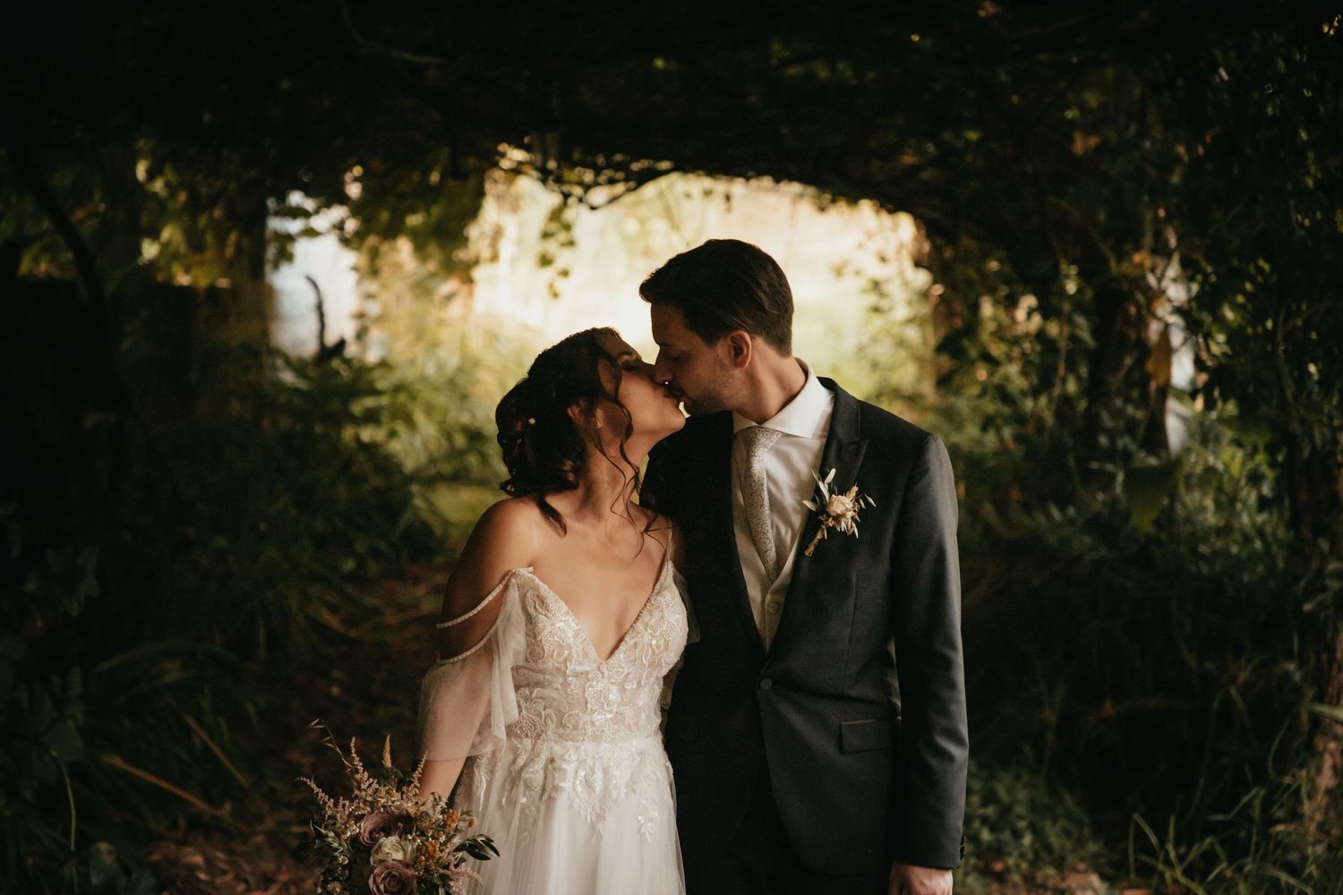 Intimate wedding portrait captured in a sun-dappled forest setting.