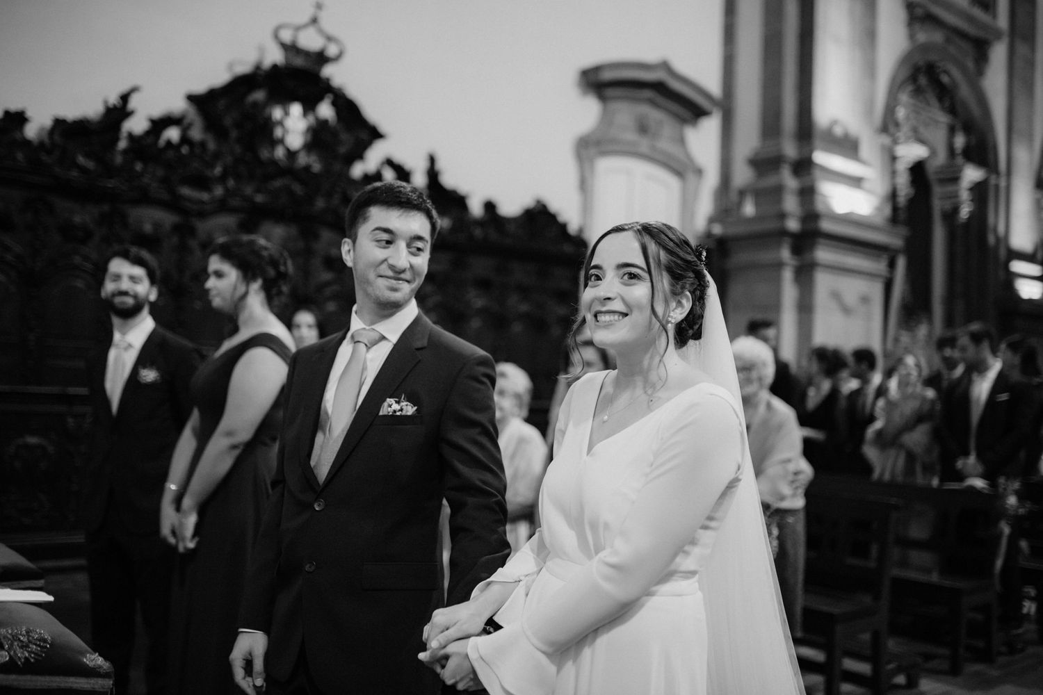 Black and white photo of a wedding ceremony with guests standing outdoors by a historic church.