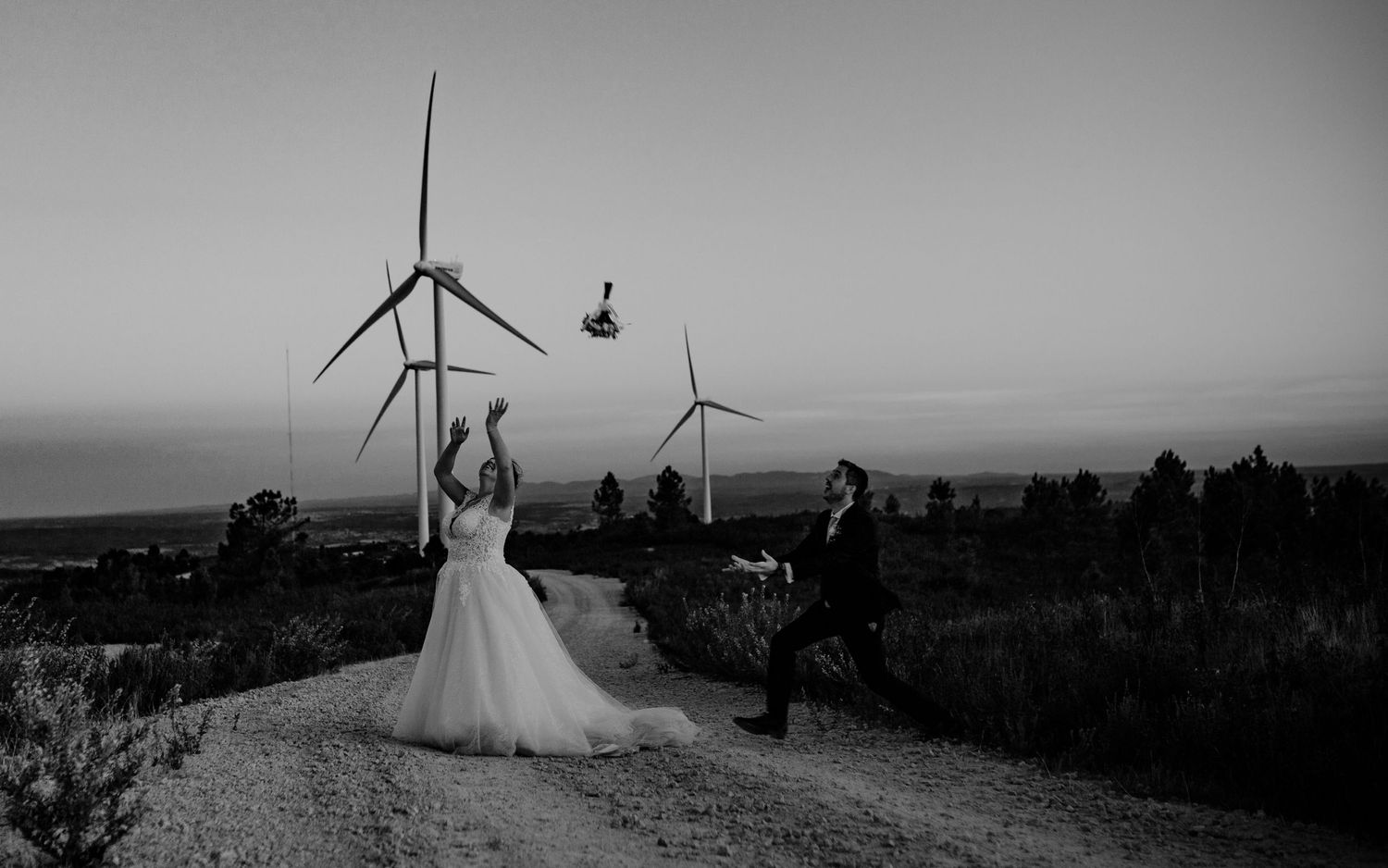 Black and white wedding photo with wind turbines creating dramatic industrial backdrop.