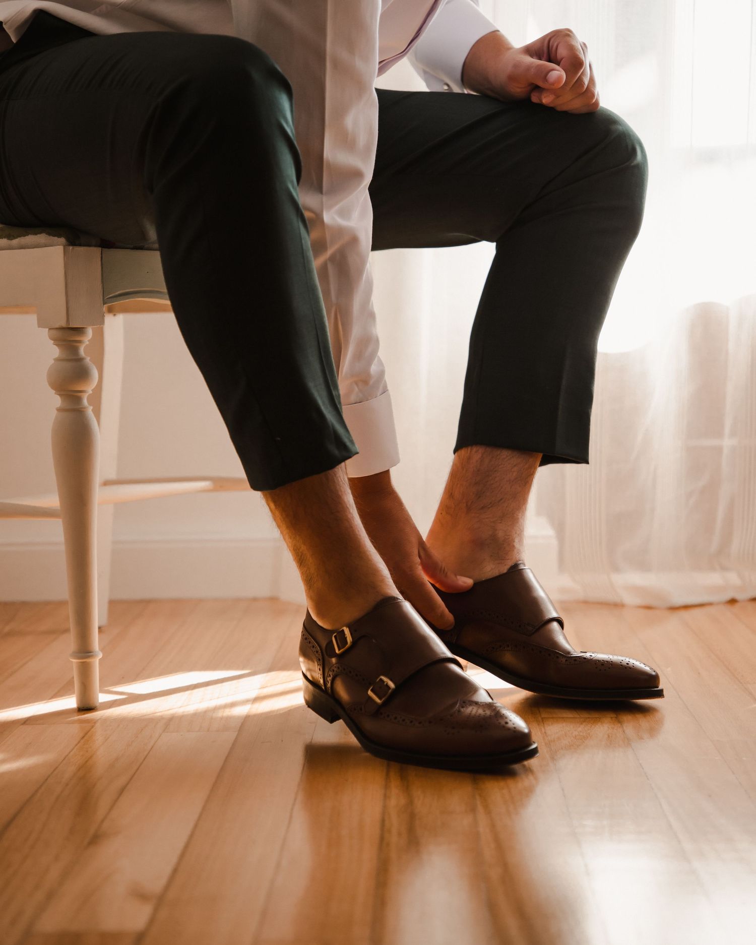 Detail shot of polished brown monk strap dress shoes and formal pants on hardwood floor.