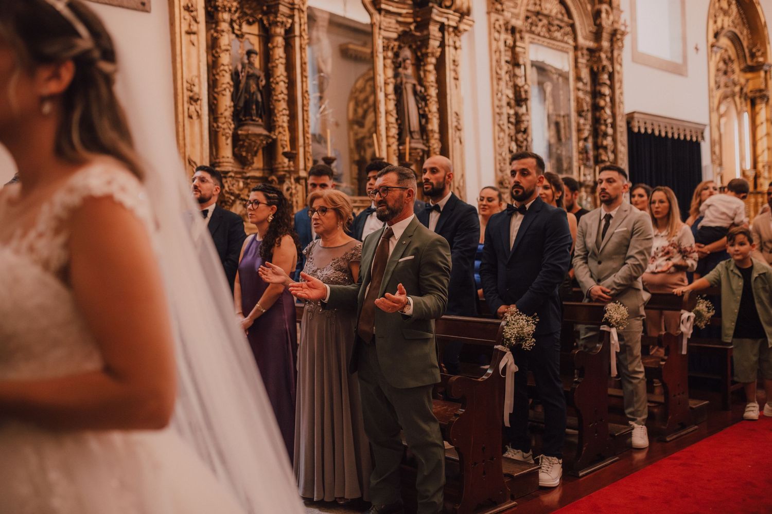 Wedding ceremony in an ornate church with decorative golden altar and guests in attendance.