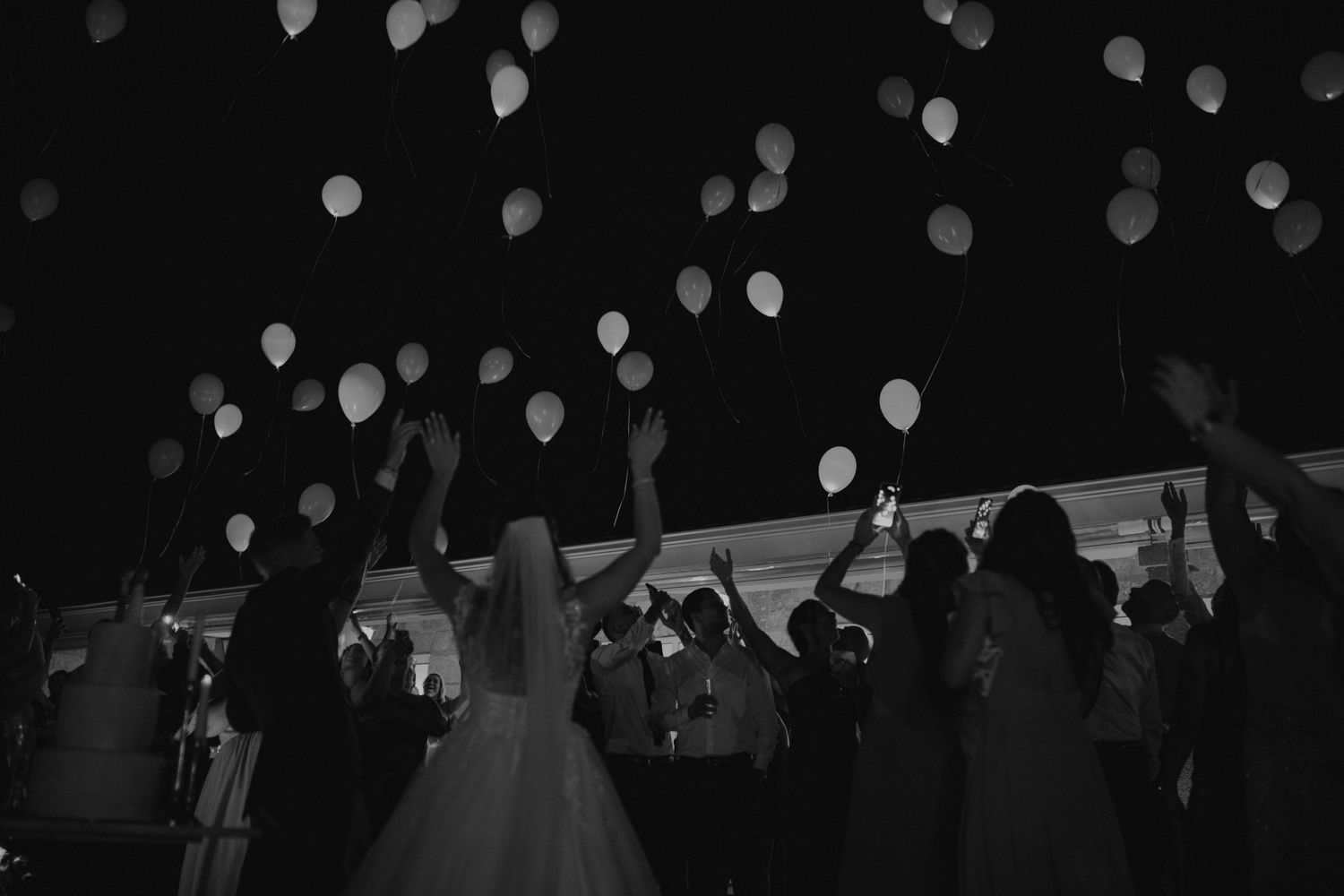 Wedding guests release glowing balloons into the night sky during an outdoor celebration.