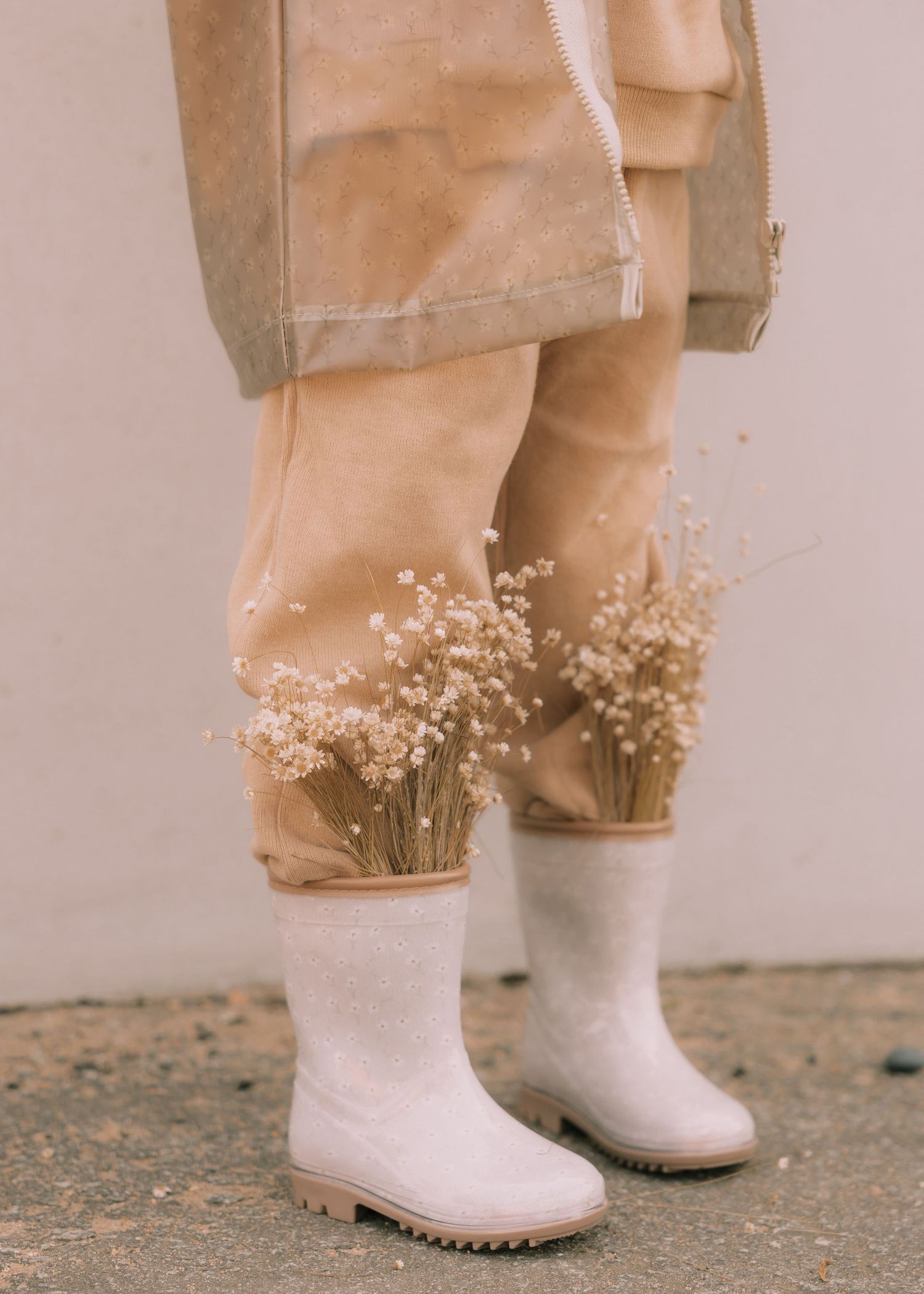 Close-up view of white rubber boots with delicate dried flowers arranged against a beige background.