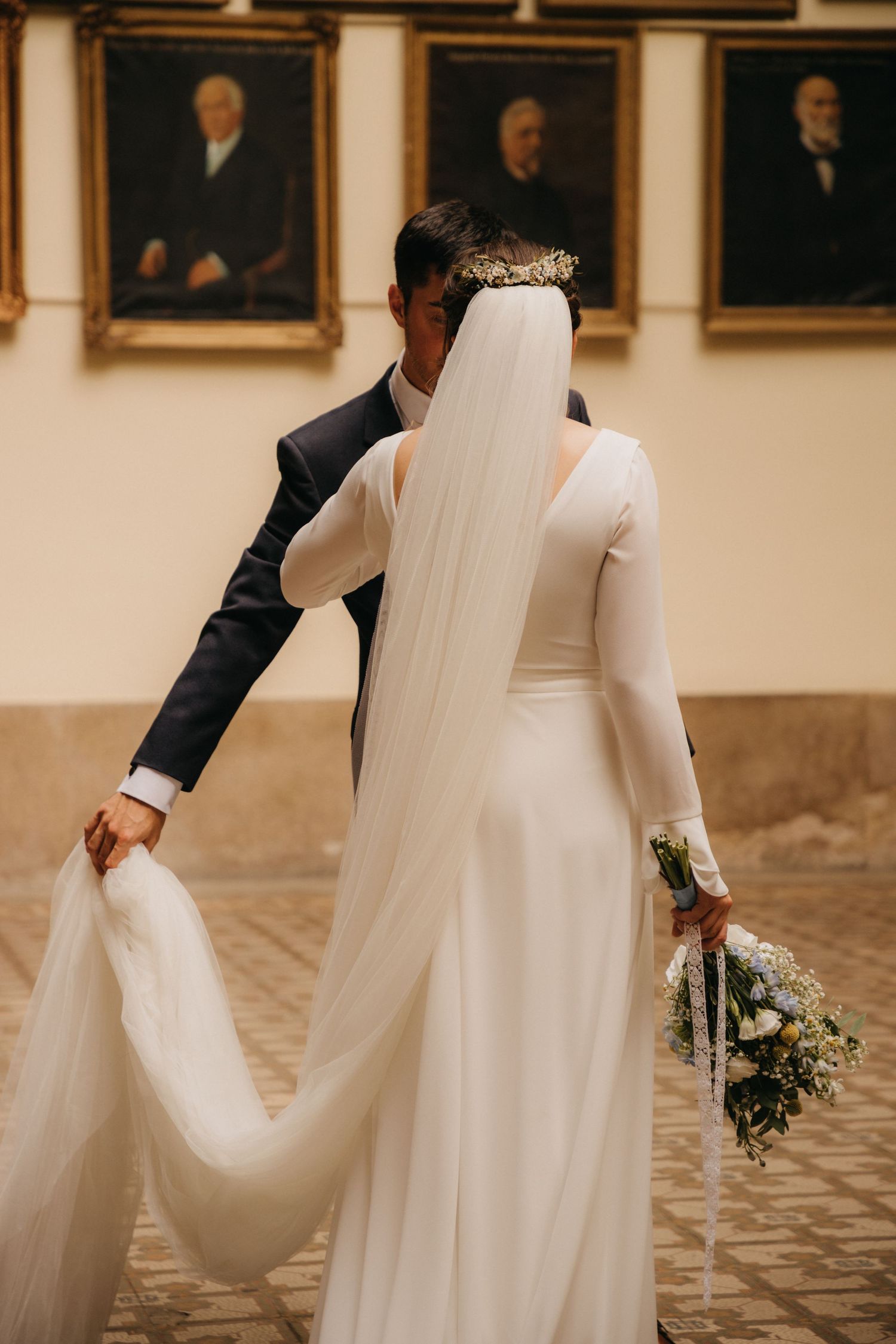 Artistic shot of bride in elegant long-sleeved gown with flowing veil against gallery wall.