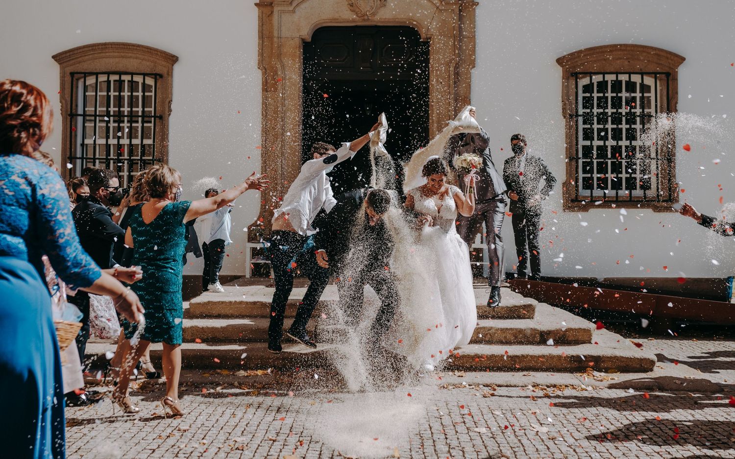 Joyous wedding scene with confetti flying as couple exits historic church building.