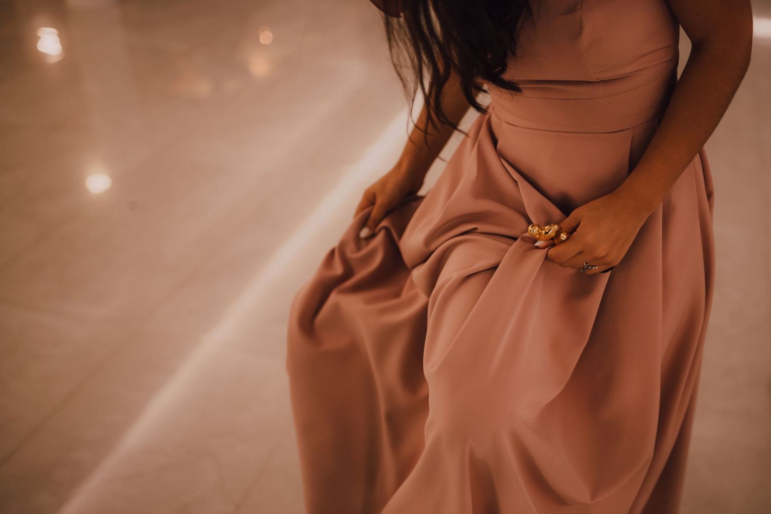Close-up detail of a flowing dusty rose bridesmaid dress in soft reception lighting.