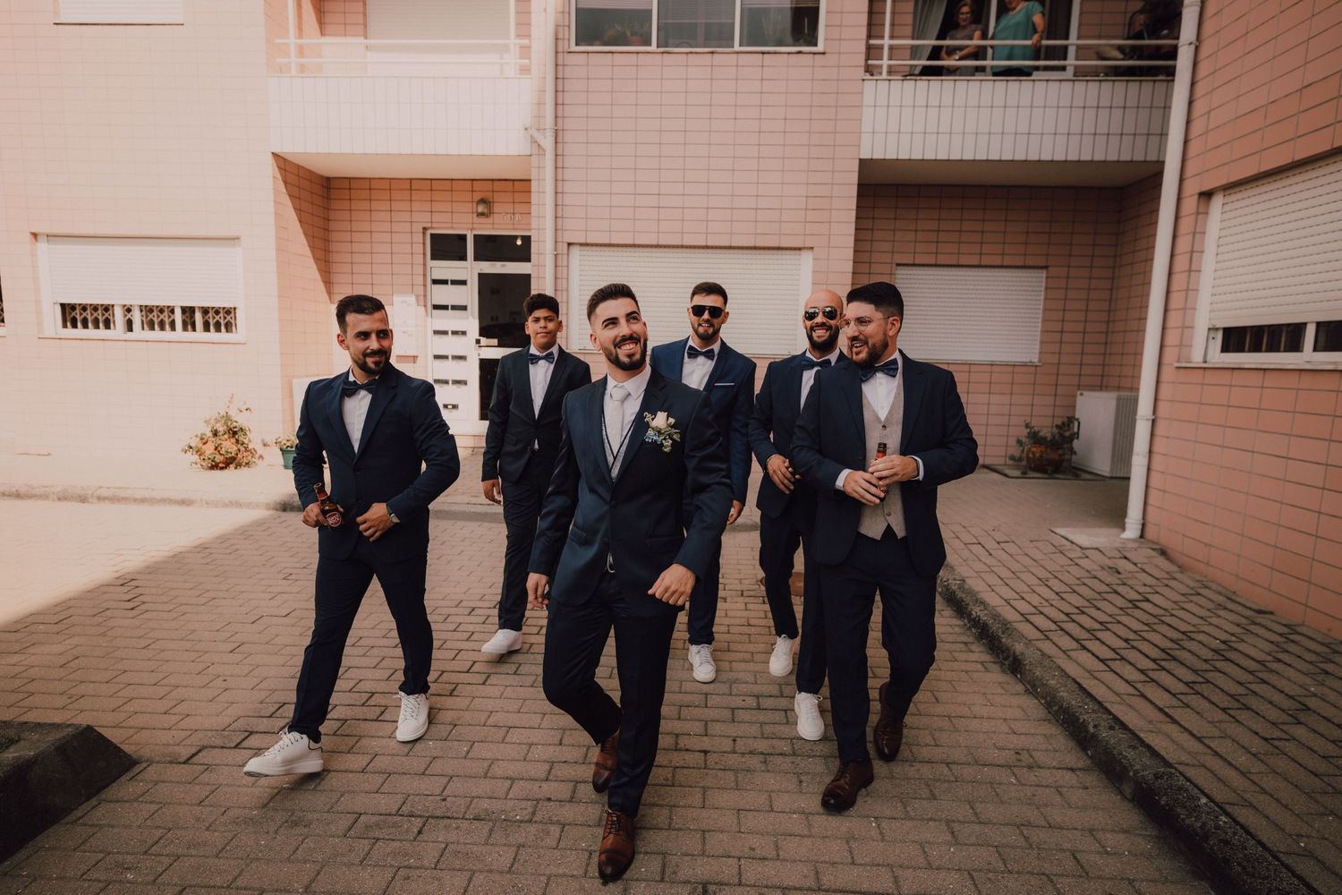 A group in formal attire walks together on a paved pathway outside a building.