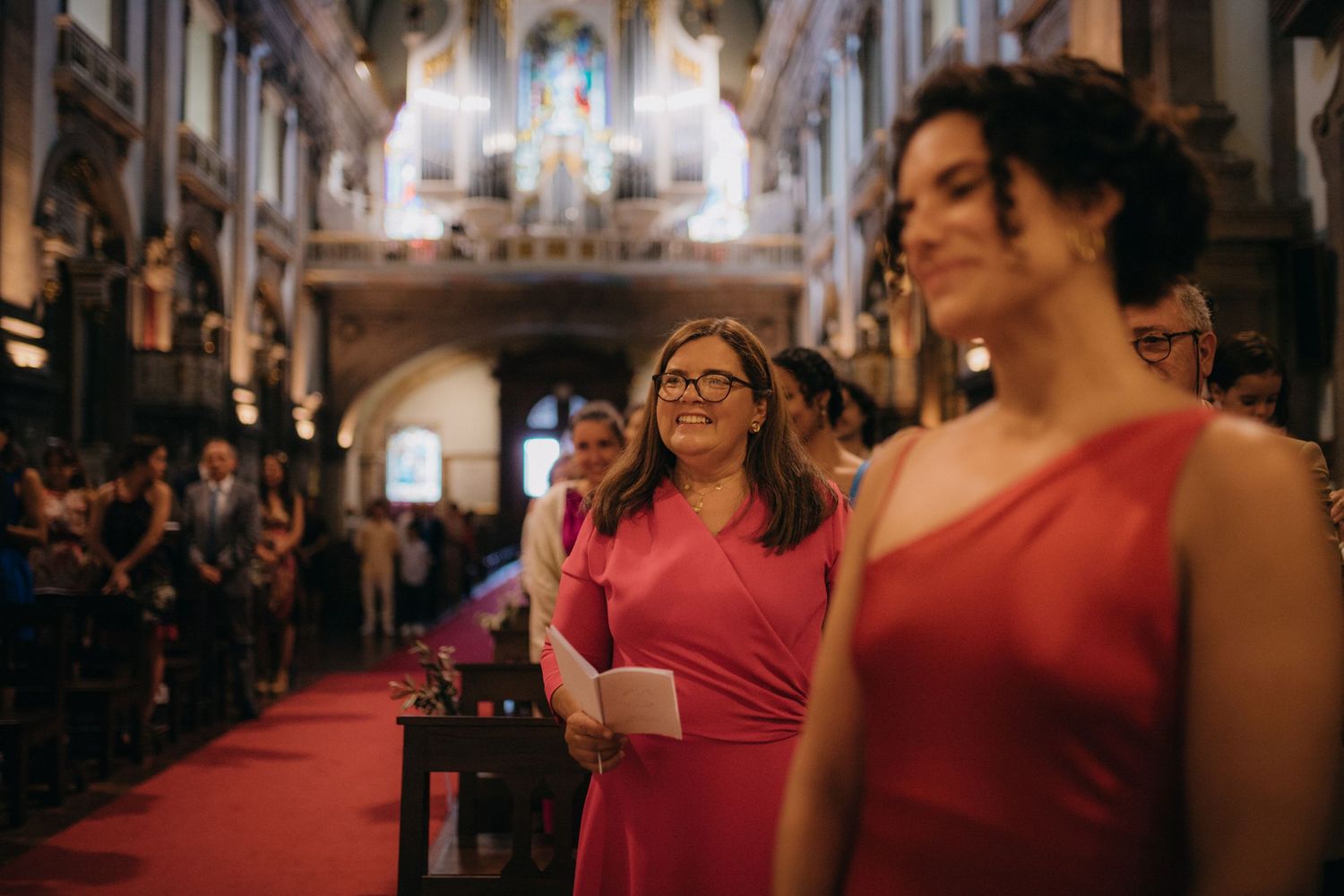 Wedding guests in formal attire standing in ornate church with vaulted ceilings.