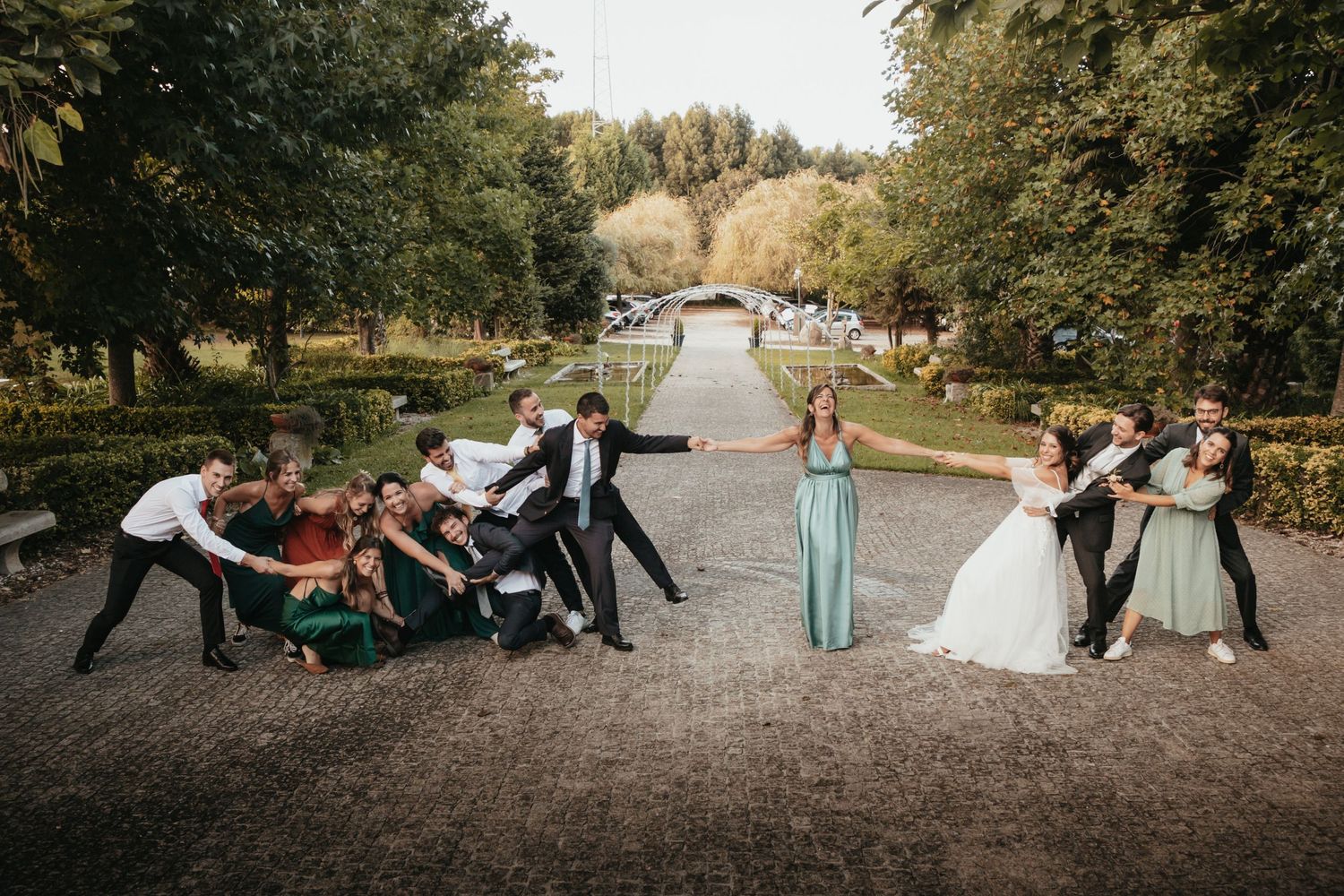 Playful wedding party poses for a fun group photo in a garden setting.