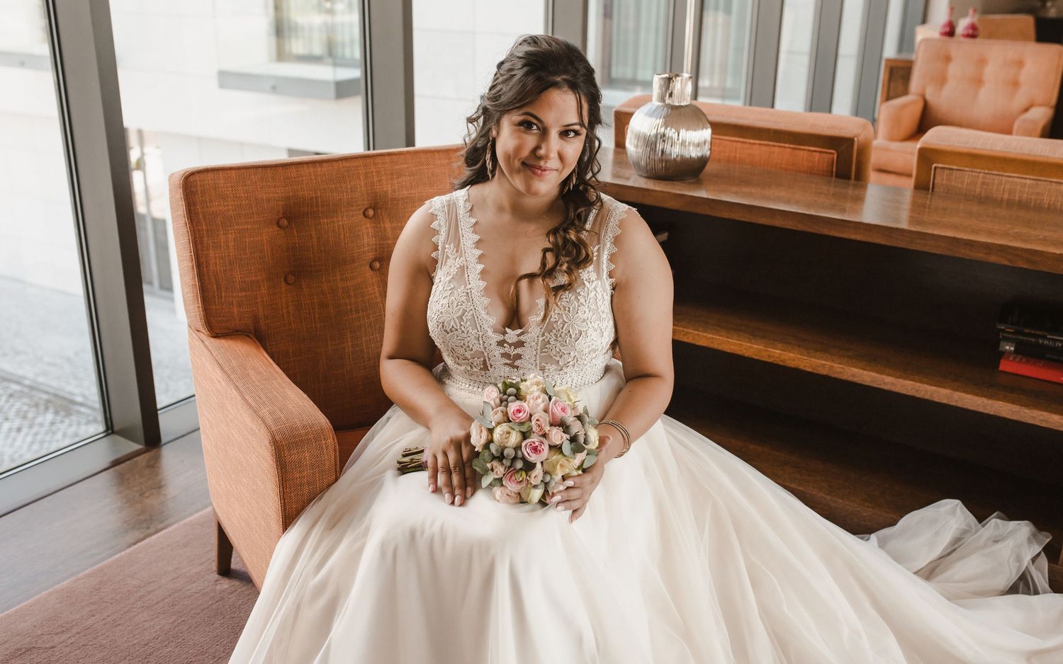 Wedding dress detail with delicate lace and floral bouquet in sunlit room.