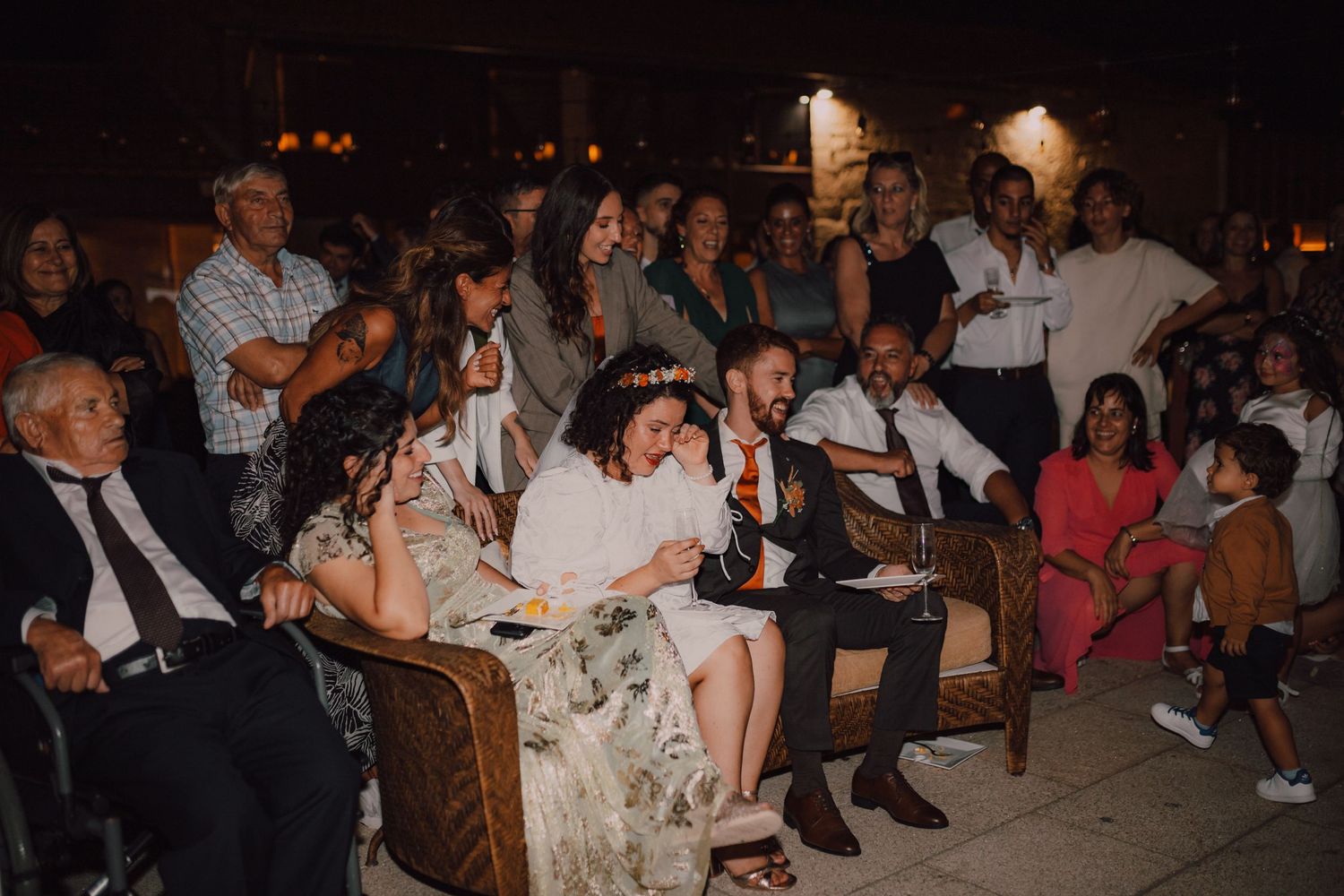 Wedding guests seated in chairs watch the celebration during an outdoor evening reception.