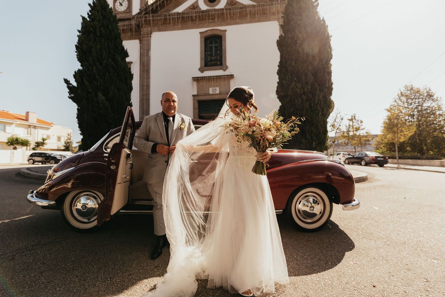 Beautiful bridal moment next to classic vintage car outside historic building.