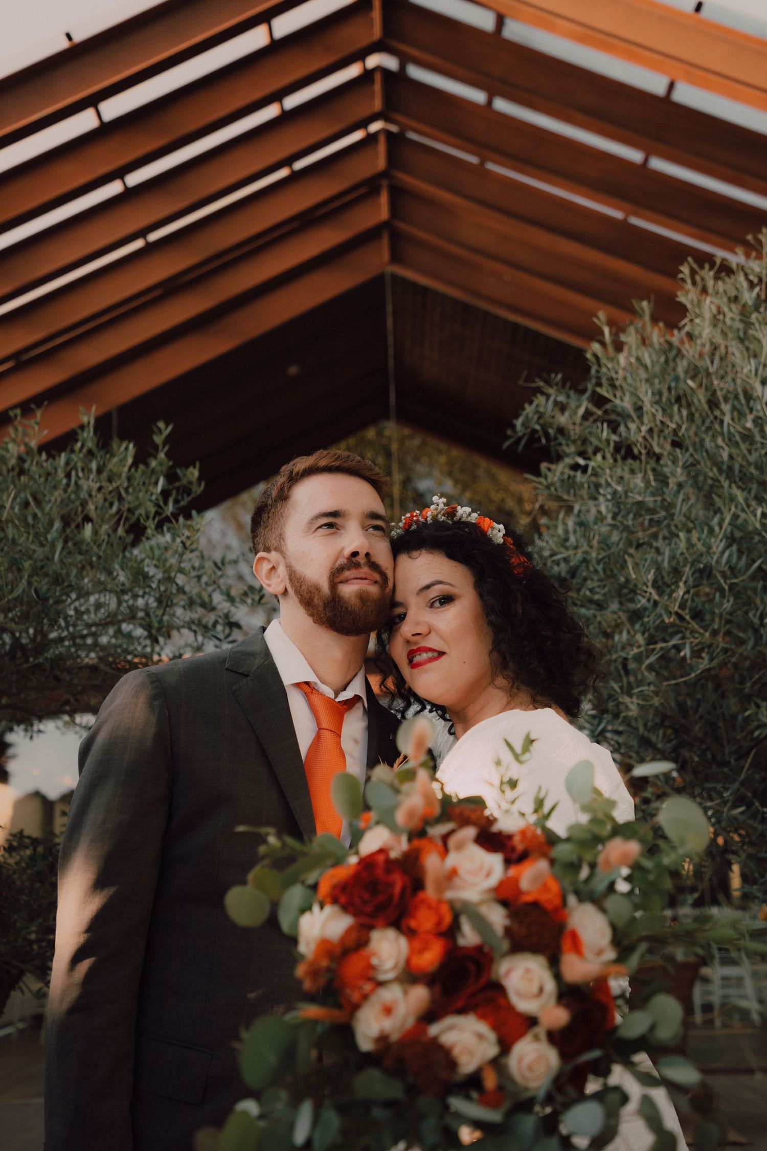 Sunset wedding portrait with orange florals and eucalyptus bouquet under wooden beams.