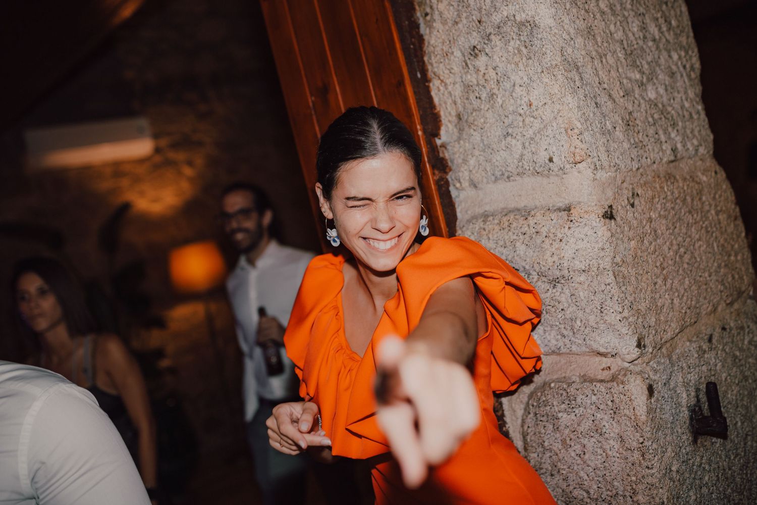 Wedding guest in vibrant orange dress dancing and smiling during reception.