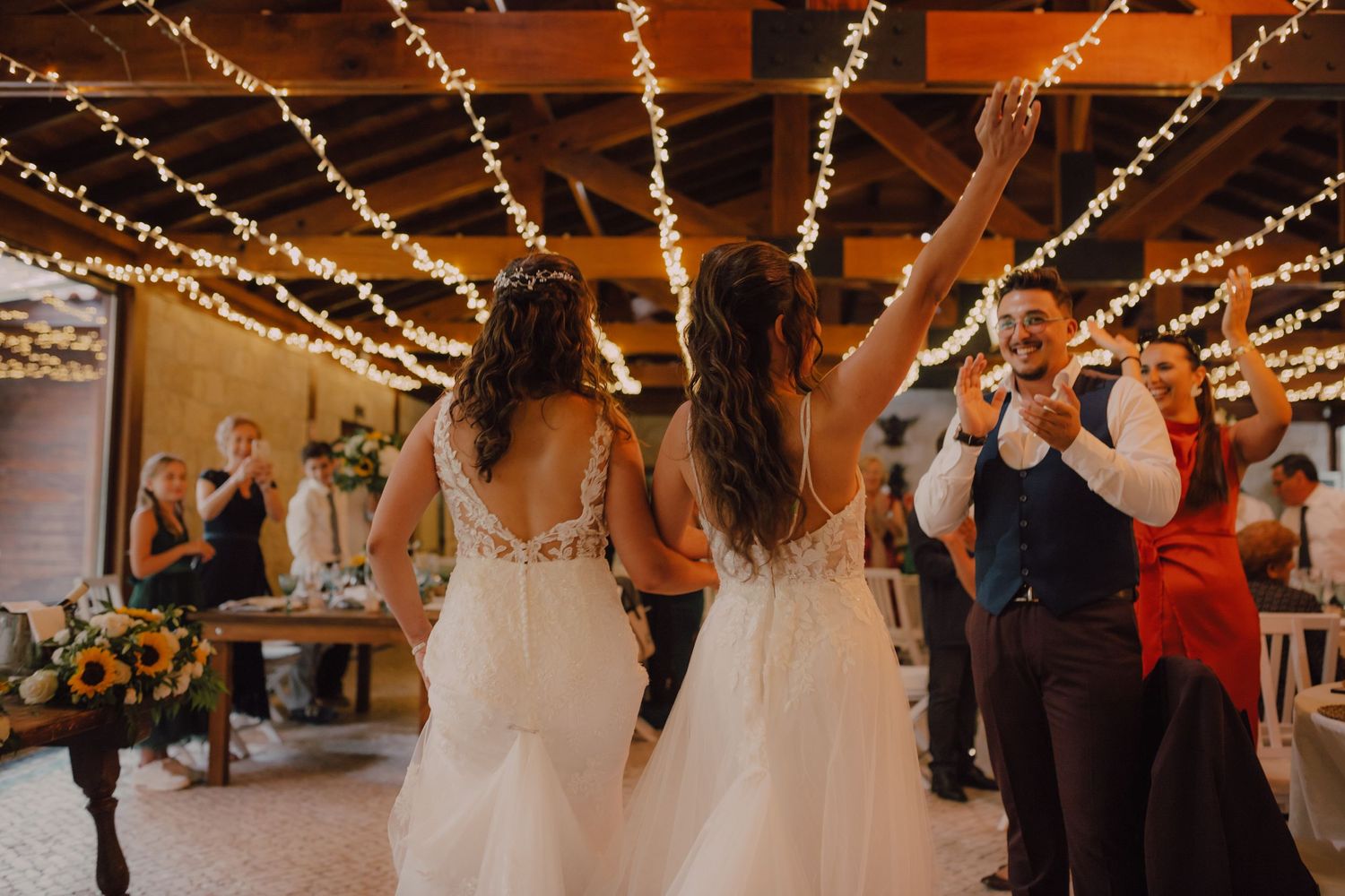 Wedding guests dance under warm string lights at indoor reception venue.