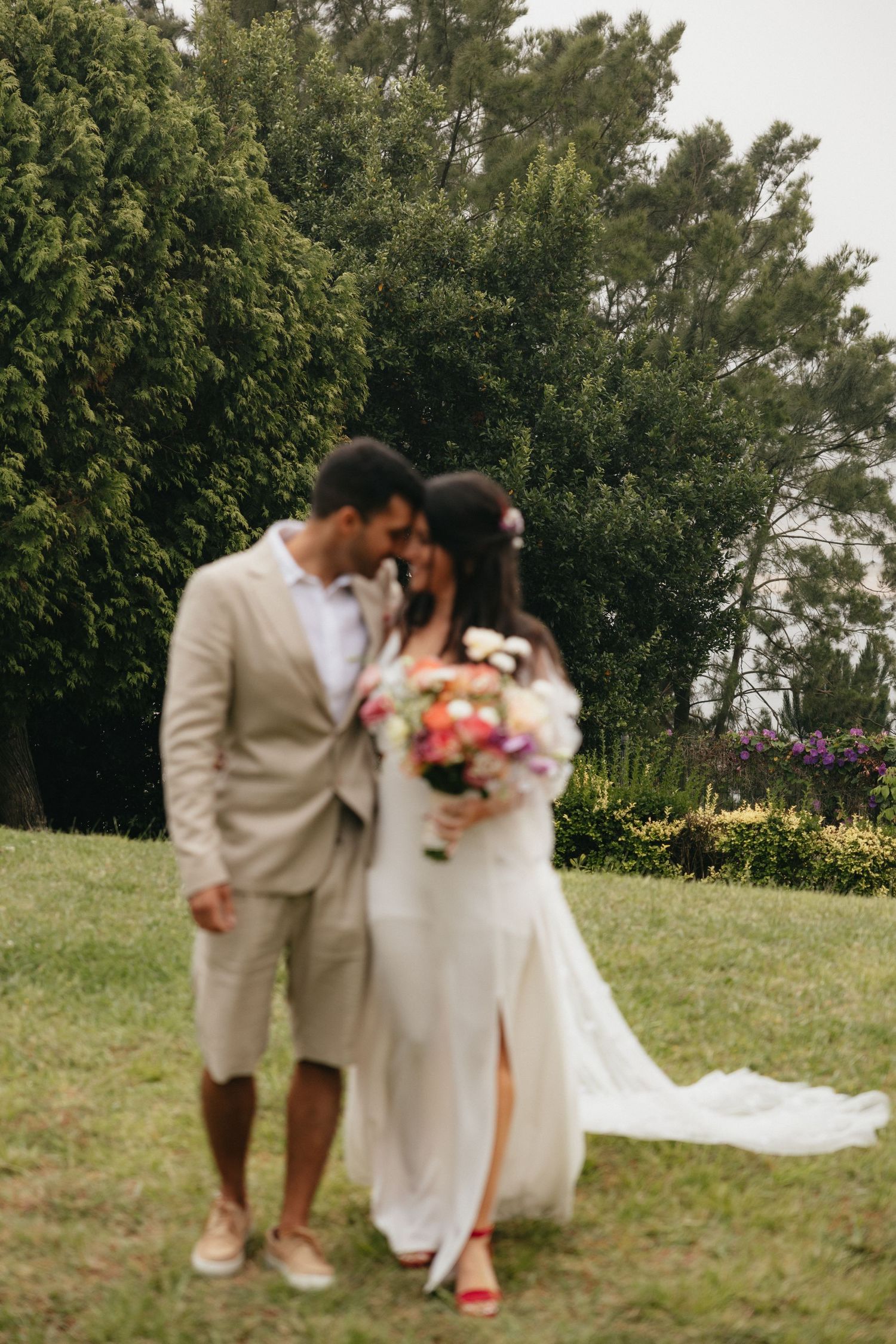 Wedding couple standing in lush garden setting with colorful bouquet.