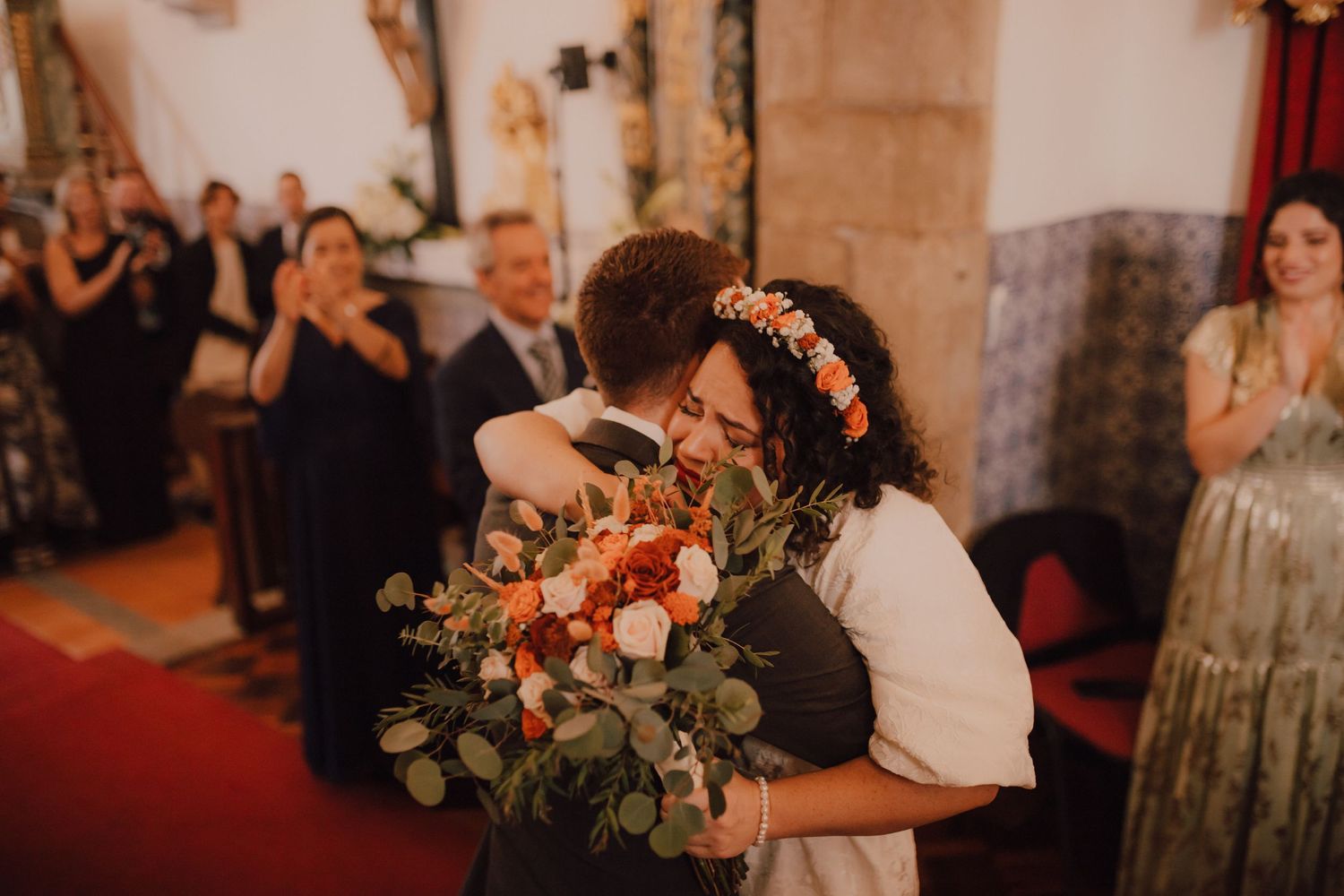 A warm embrace shared during a wedding ceremony in a historic church with guests looking on.