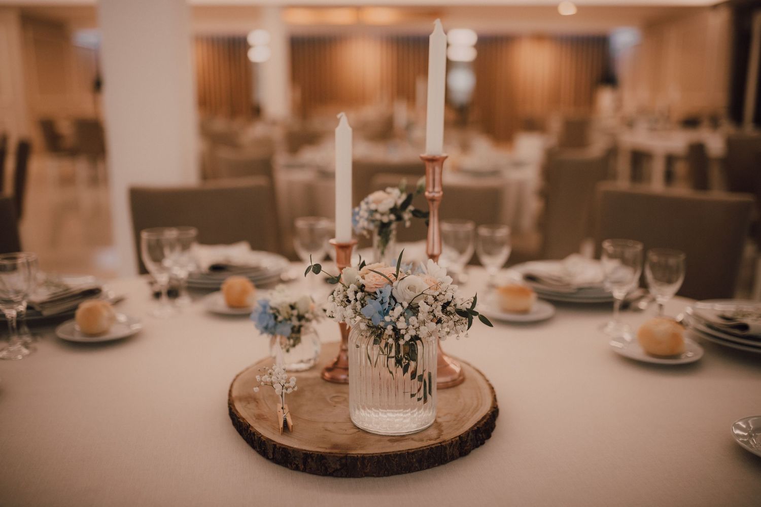 Wedding table centerpiece featuring glass bottles with flowers on a wooden disc base.