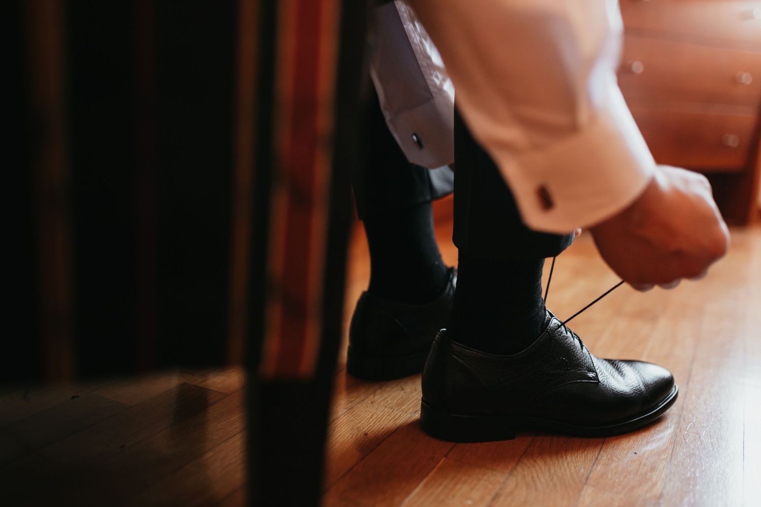 Close-up of hands tying formal black dress shoes on wooden floor.