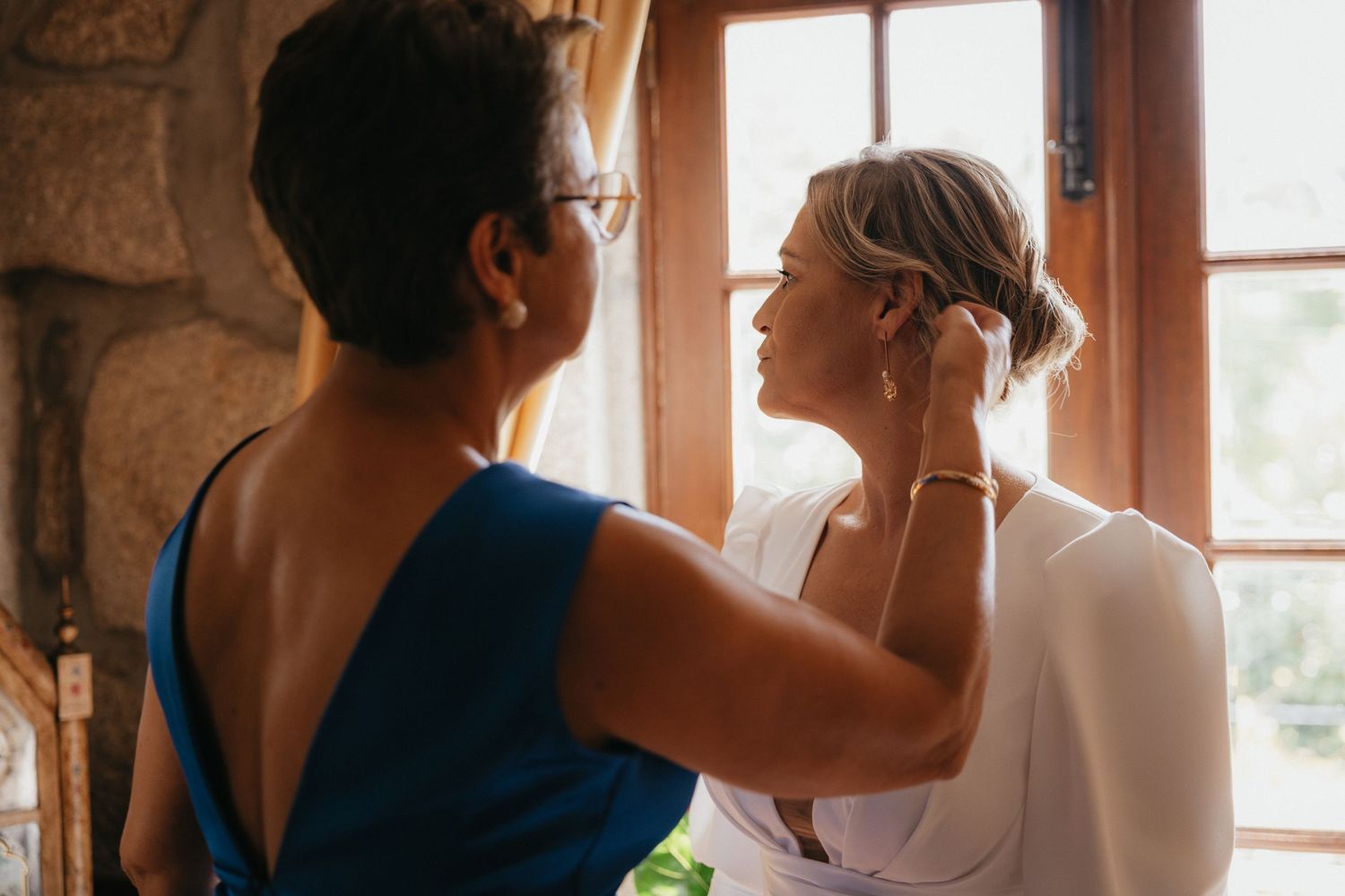 Getting ready moment in front of a sunlit window before the wedding ceremony.