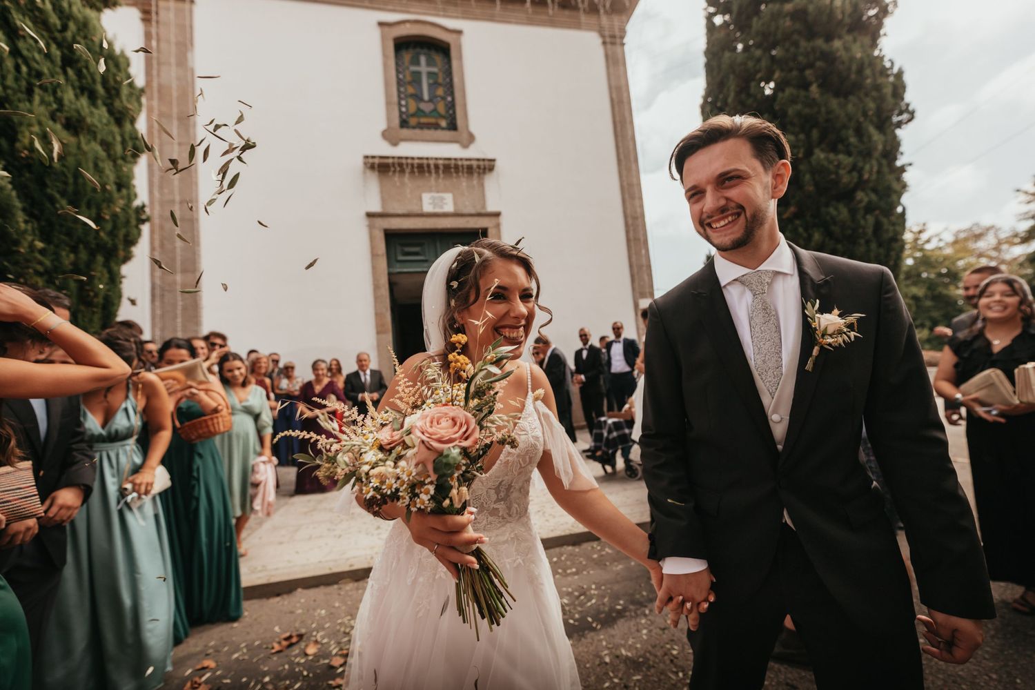 Happy couple celebrates while exiting church ceremony as guests toss confetti.