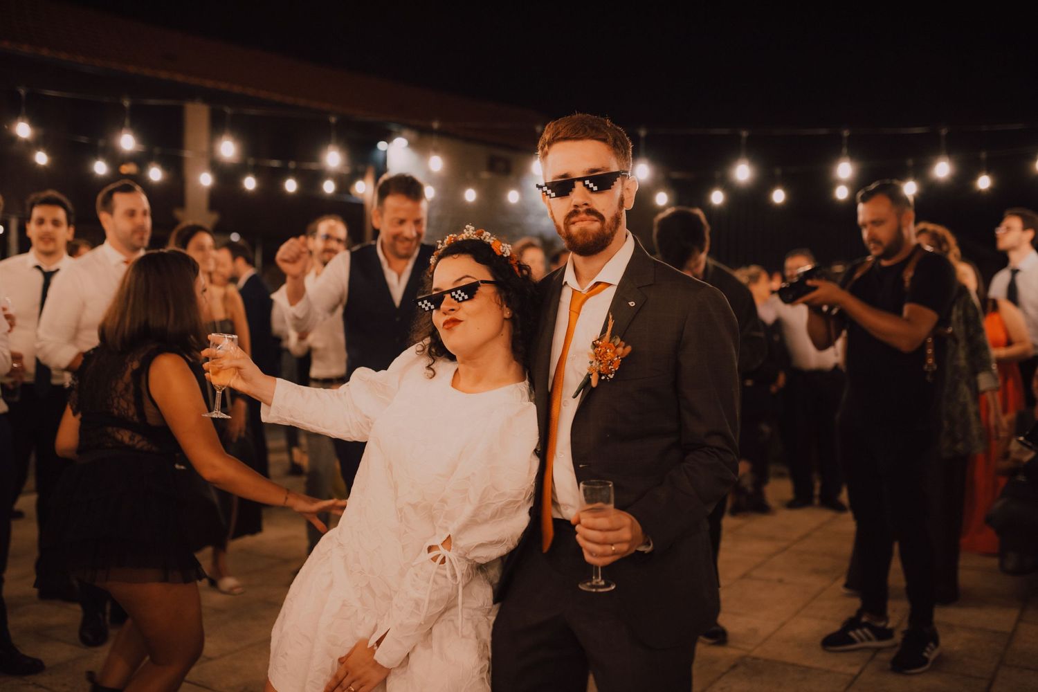 Wedding reception under string lights with guests dancing at outdoor venue.