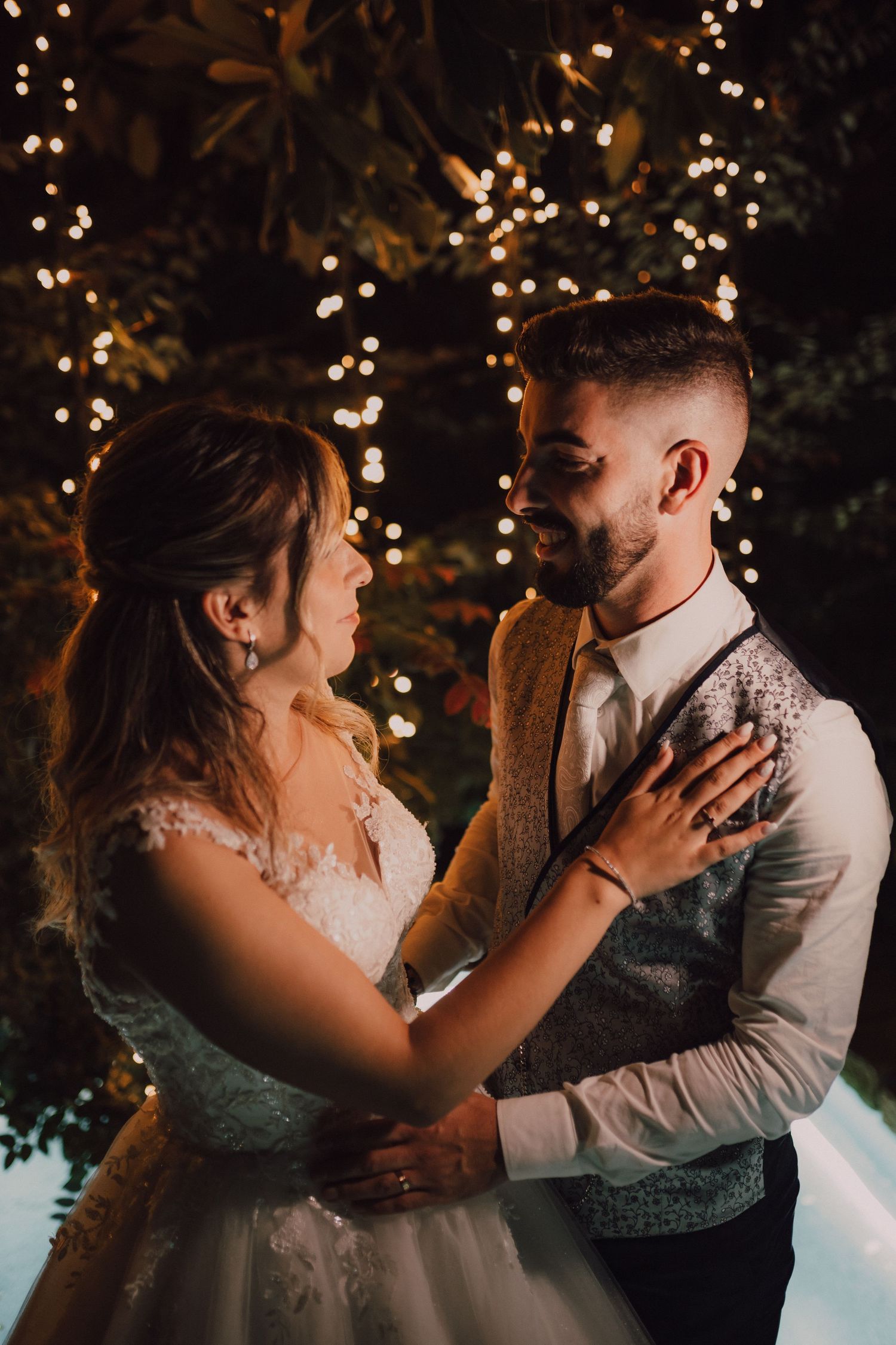 Newlyweds share intimate moment under twinkling lights during evening wedding reception.