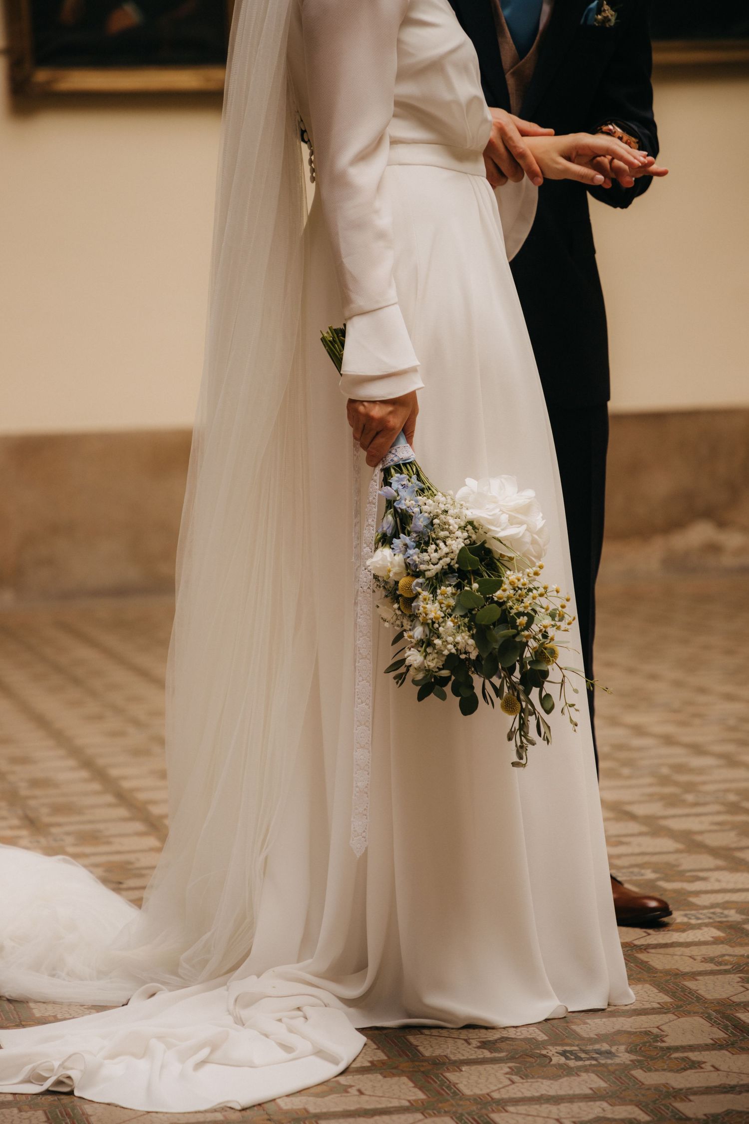 A white wedding dress with long sleeves and a flowing train while holding a delicate floral bouquet.