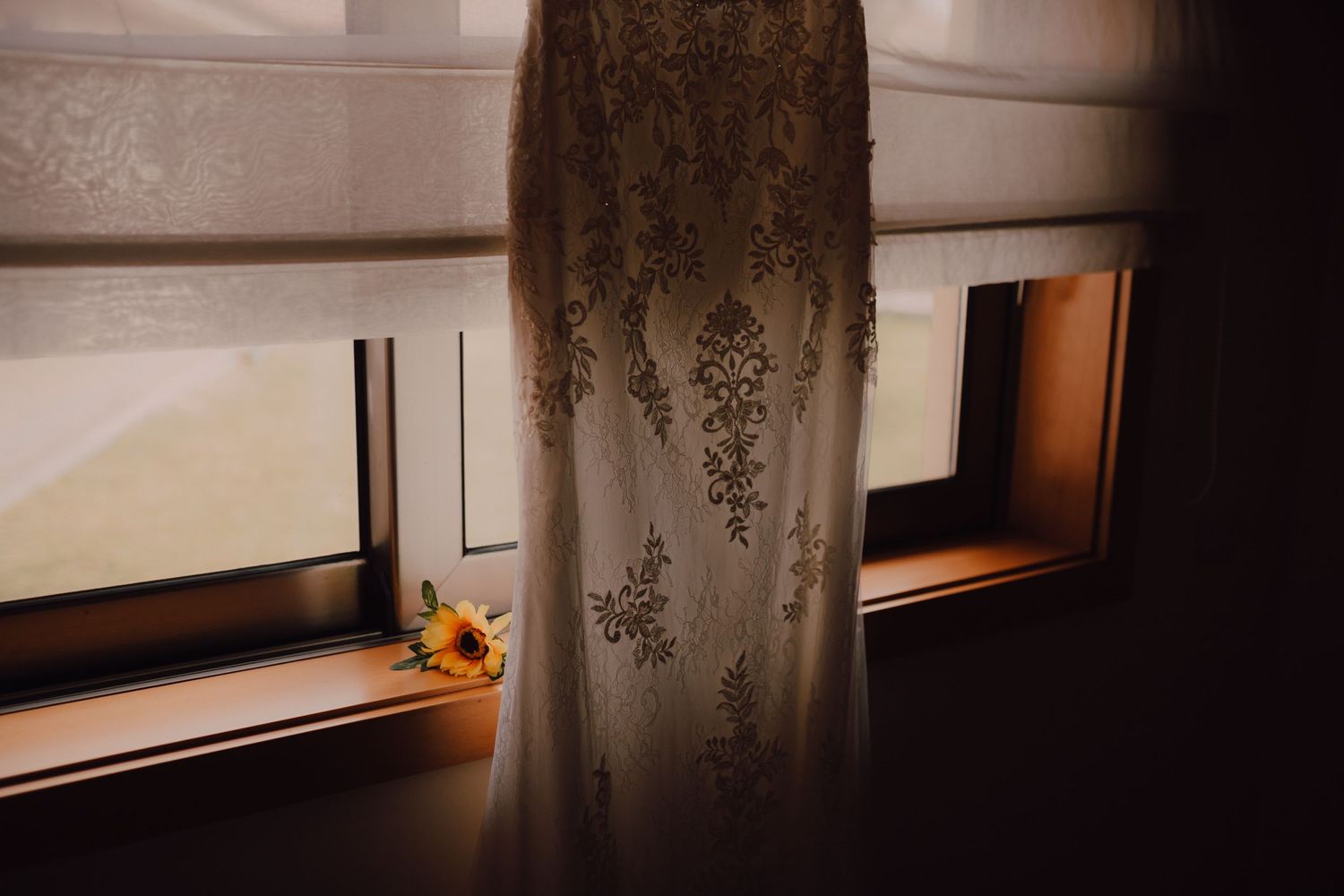 Detail shot of intricate lace wedding dress hanging by window with sunlight.