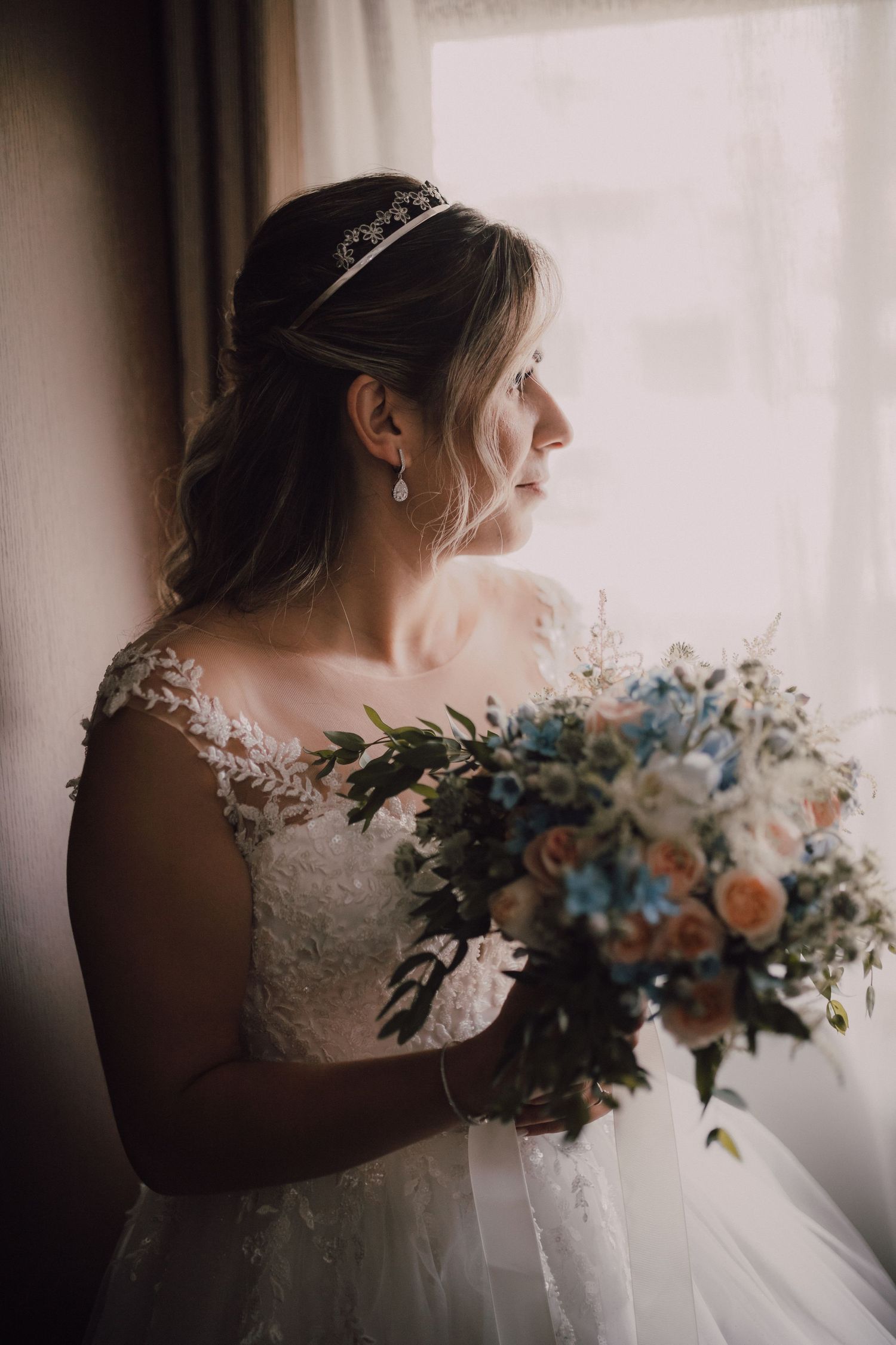 Wedding bouquet with blue and peach flowers held by someone in a detailed lace wedding dress.