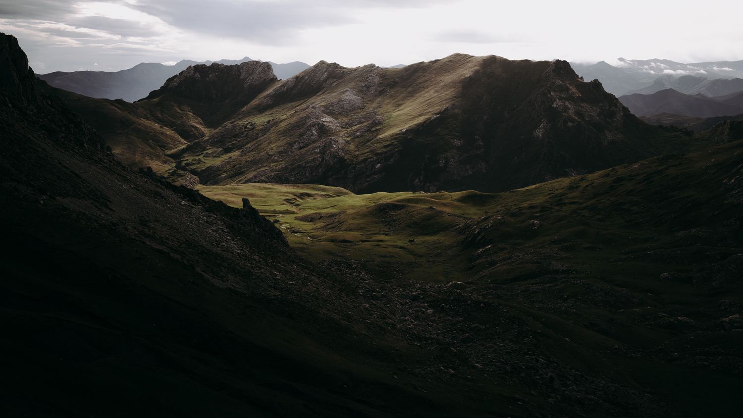 Dramatic mountain landscape with rolling hills and valleys under moody clouds.