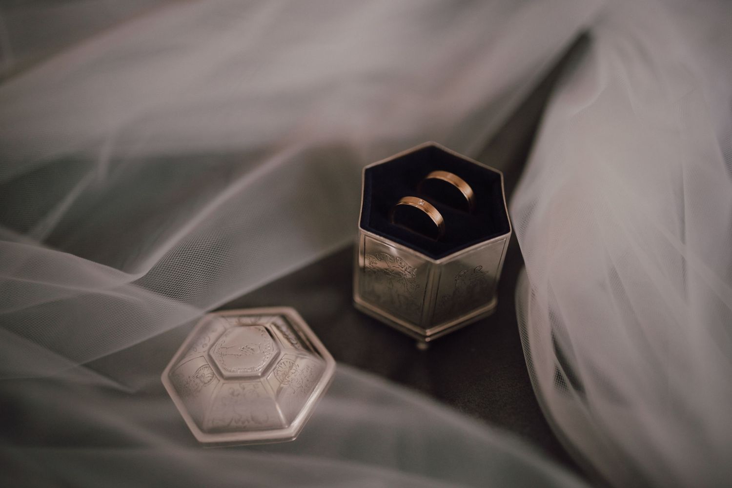 Wedding rings displayed in hexagonal box on white tulle fabric.
